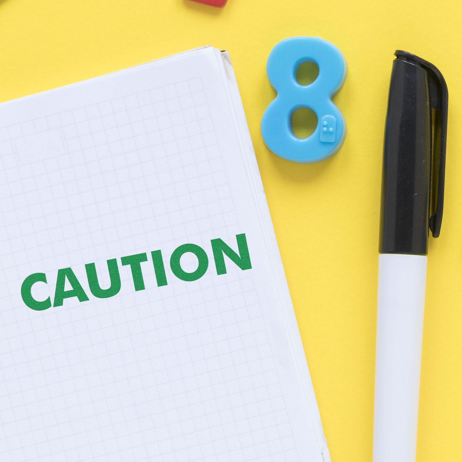 Caution Rubber Stamp imprint on a notebook with a black pen and a blue number 8 magnet on a yellow background.