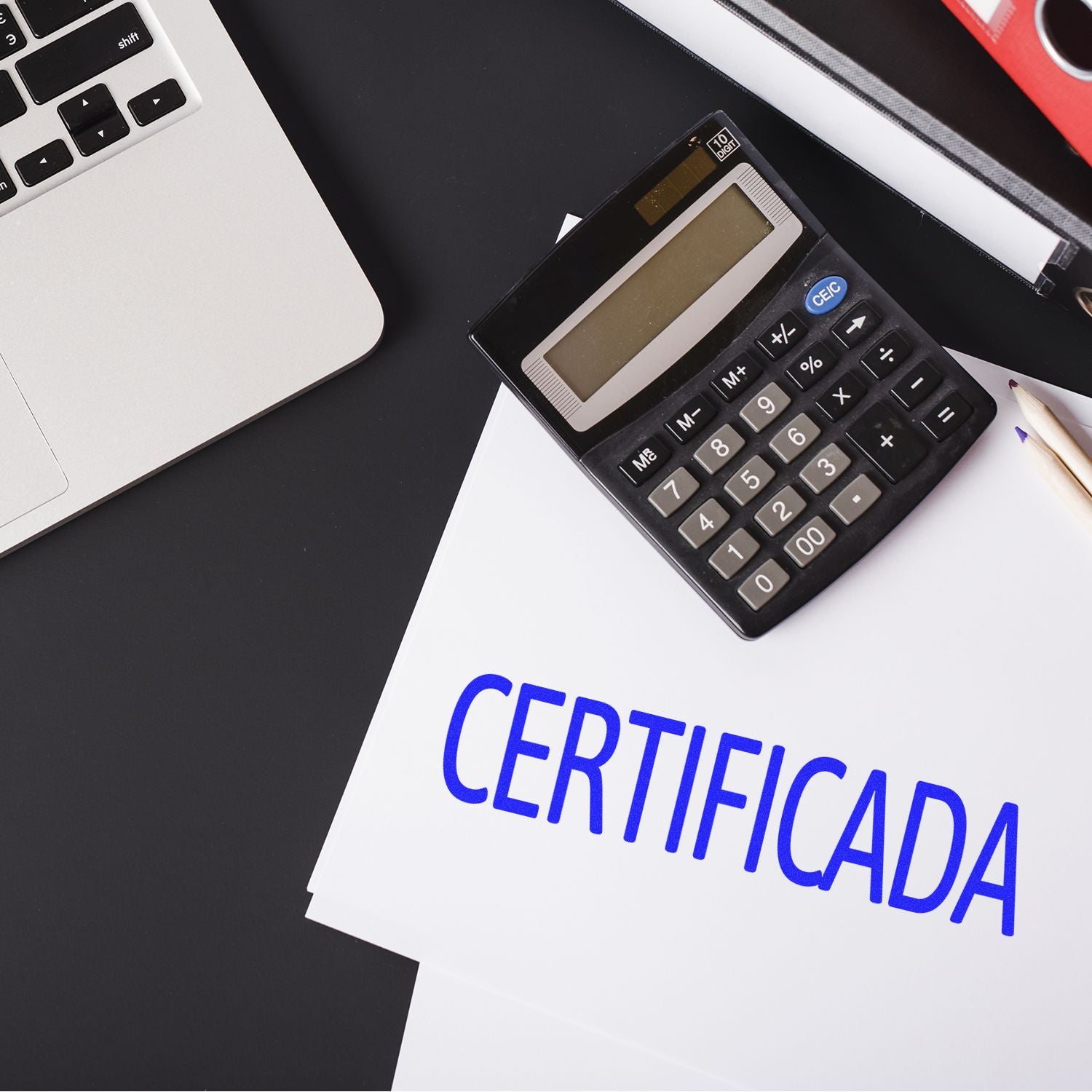 A Large Certificada Rubber Stamp imprint on a document next to a calculator, pencil, and a laptop on a black desk.