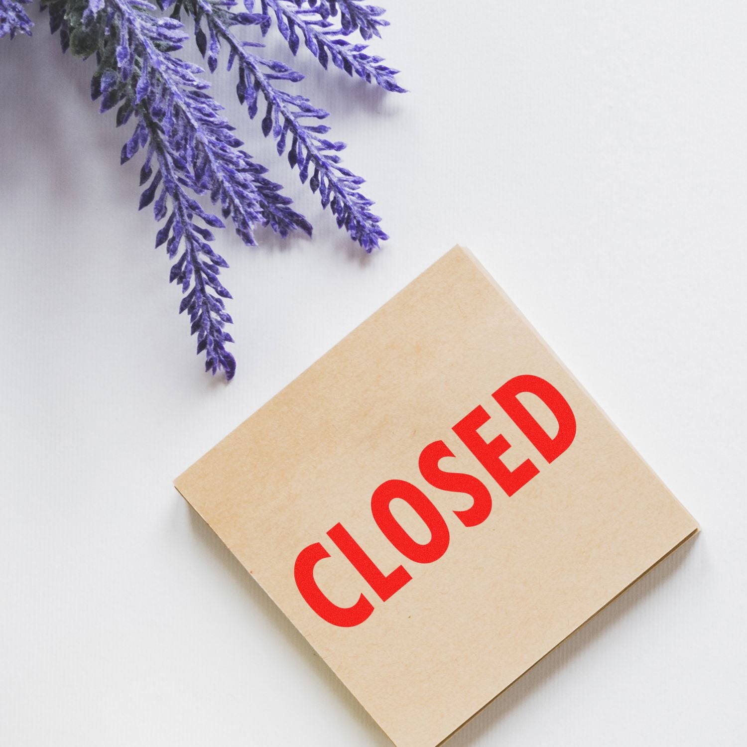 Self Inking Closed Stamp in red on a beige square card, placed on a white surface with purple lavender flowers in the corner.