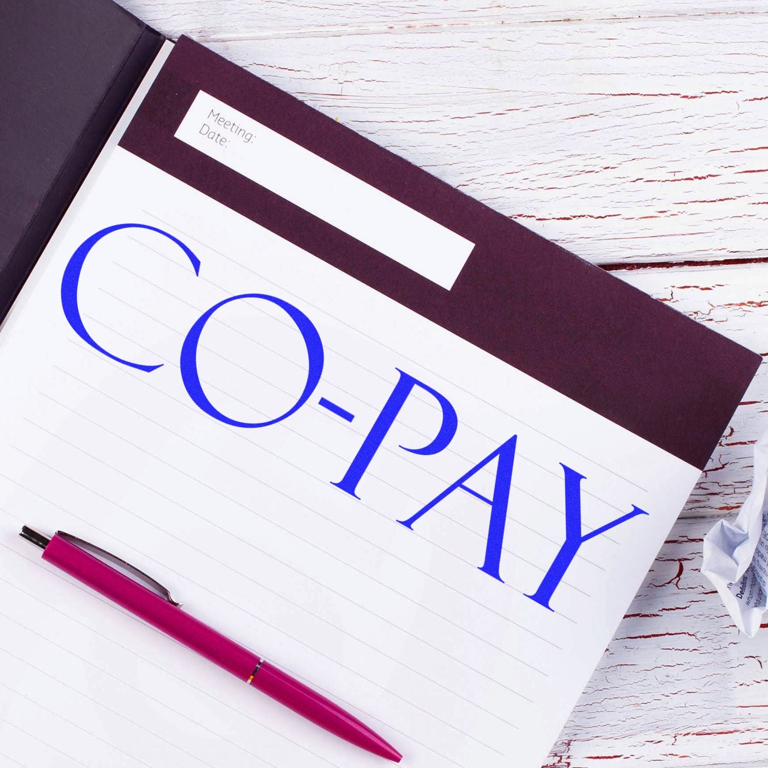 Large Co Pay Rubber Stamp used on a notebook page with a red pen beside it on a white wooden surface.