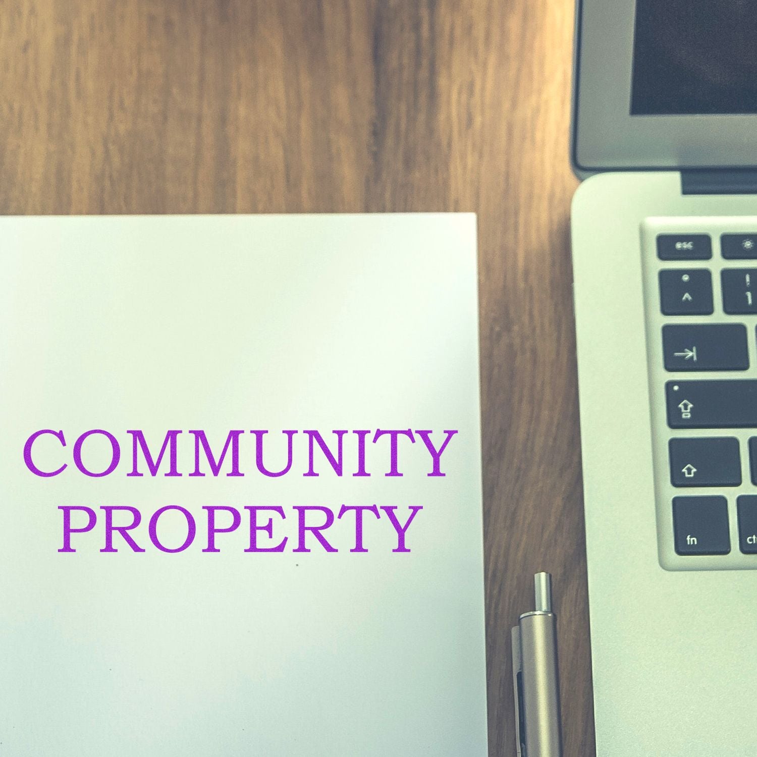 Community Property Rubber Stamp in use on a white paper beside a silver laptop and a pen on a wooden desk.