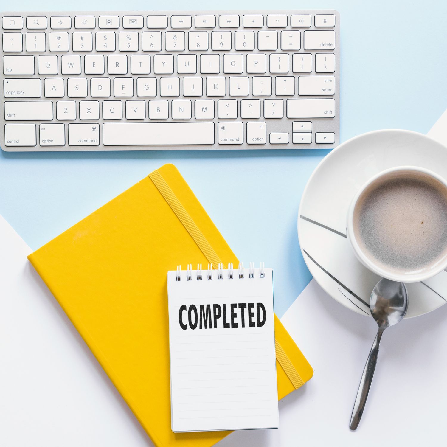 A Large Completed Rubber Stamp marks COMPLETED on a notepad, placed beside a keyboard, yellow notebook, and a cup of coffee.