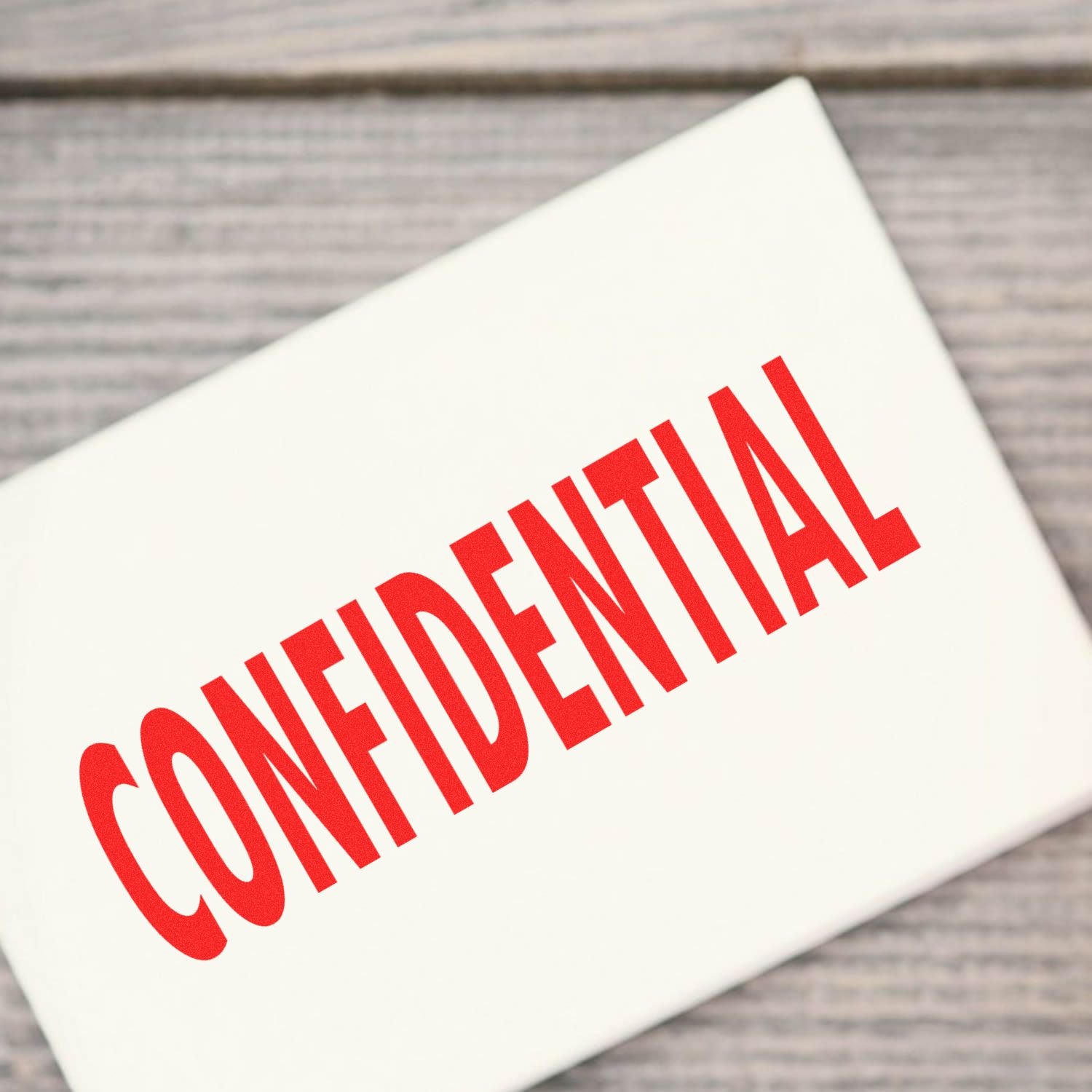 Confidential Rubber Stamp in use, displaying a bold red CONFIDENTIAL mark on a white surface, placed on a wooden background.