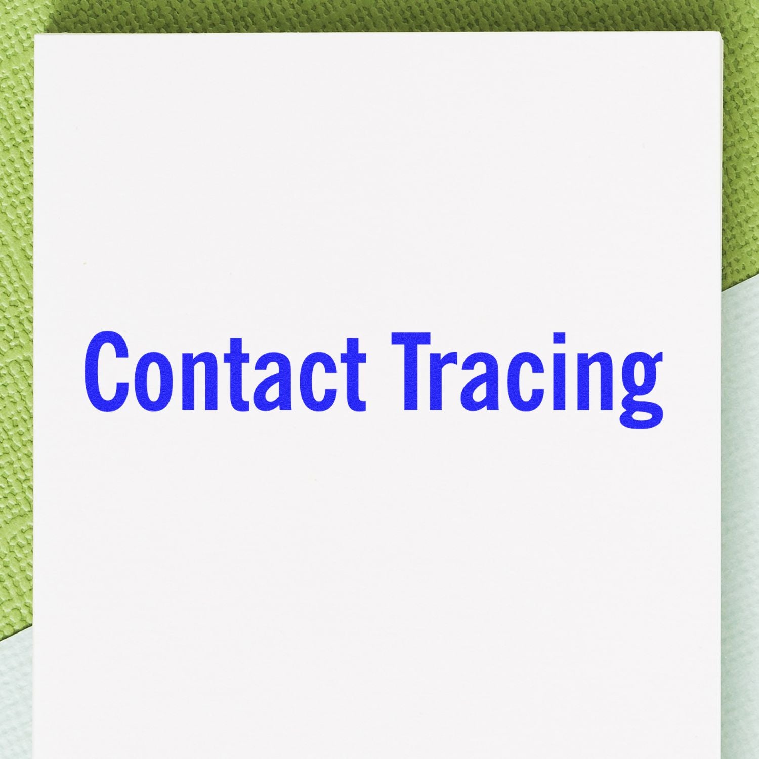 White paper stamped with 'Contact Tracing' in blue ink using the Large Pre-Inked Contact Tracing Stamp, placed on a green and white surface.