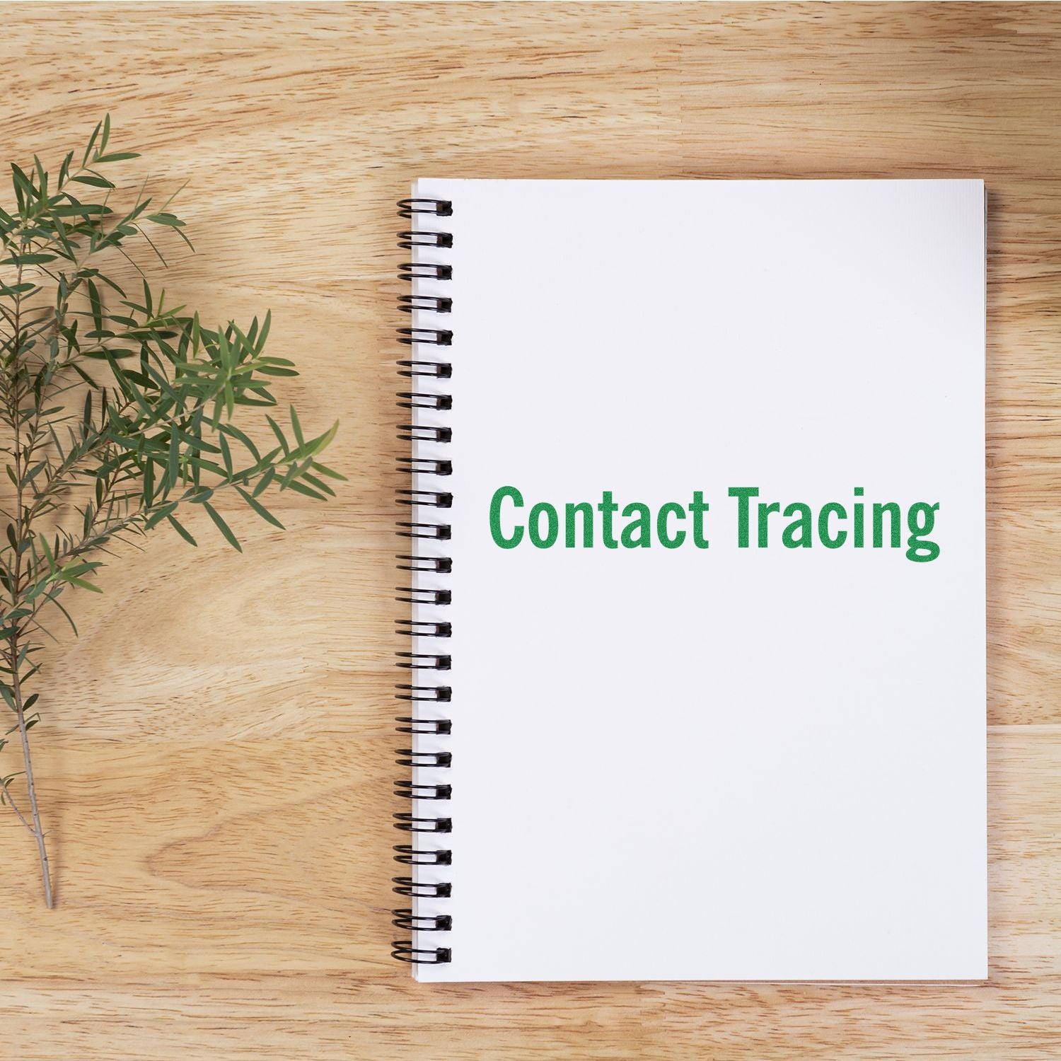 A notebook with Contact Tracing stamped in green using the Contact Tracing Rubber Stamp, placed on a wooden surface with a sprig of greenery.