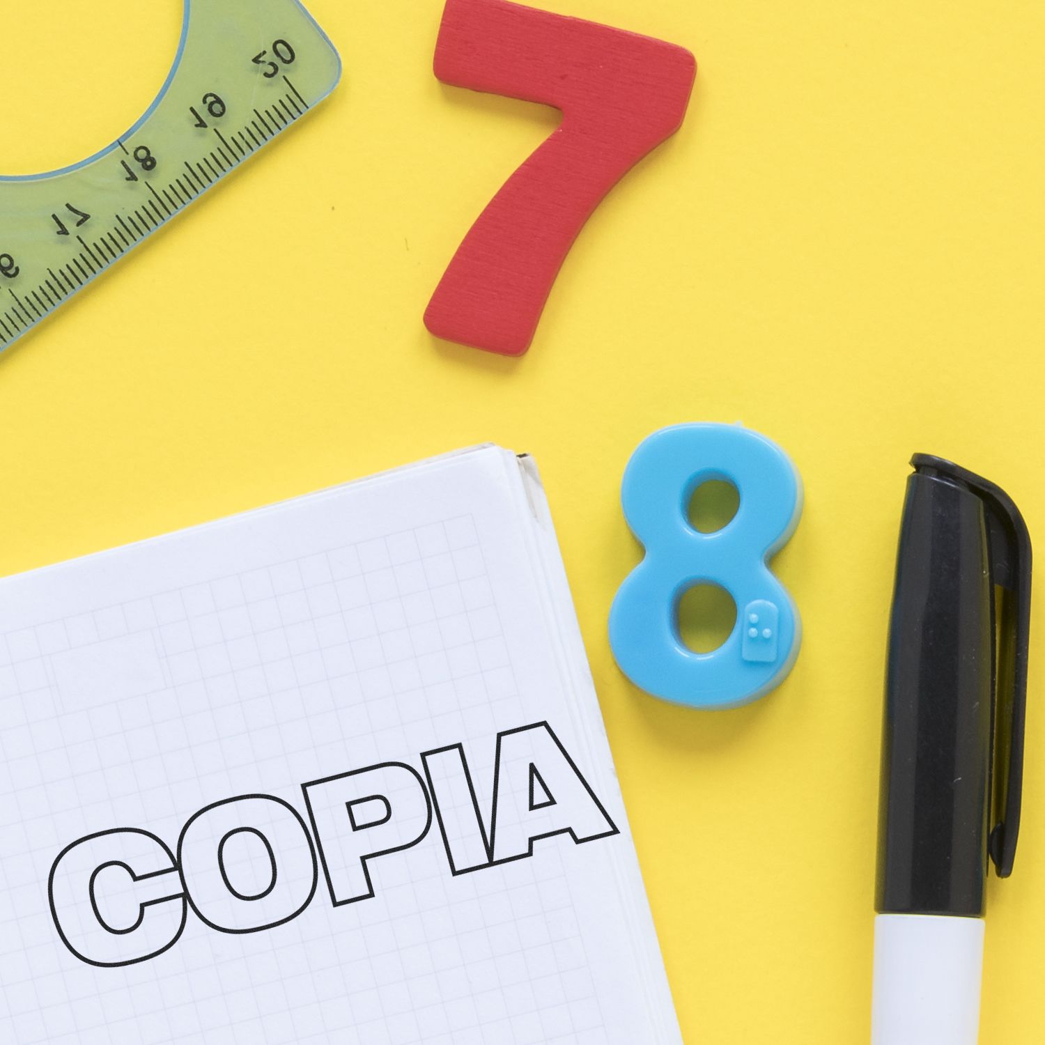 Copia Rubber Stamp on a notebook with a pen, ruler, and colorful number magnets on a yellow background.