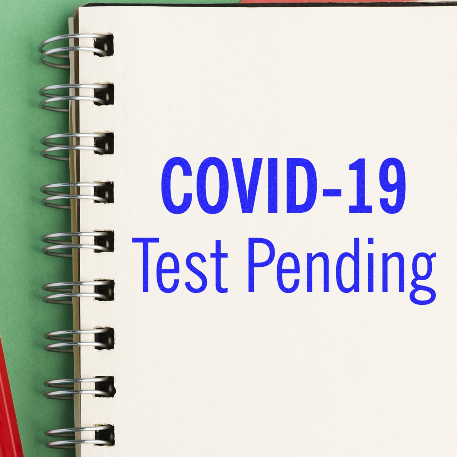 A Covid-19 Test Pending Rubber Stamp is shown on a spiral notebook with the text COVID-19 Test Pending in blue letters.