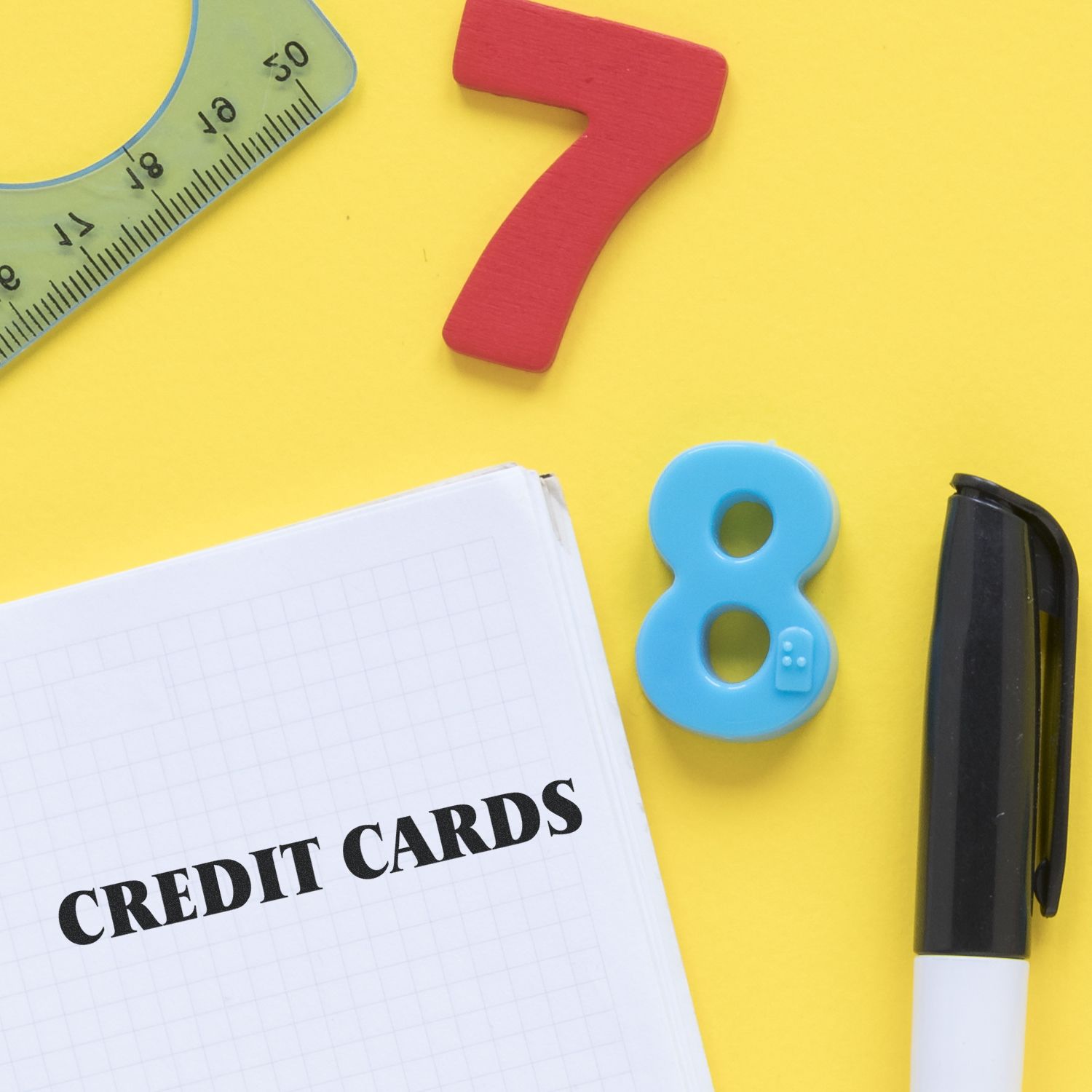 Self Inking Credit Cards Stamp on a notebook with a pen, ruler, and colorful numbers on a yellow background.