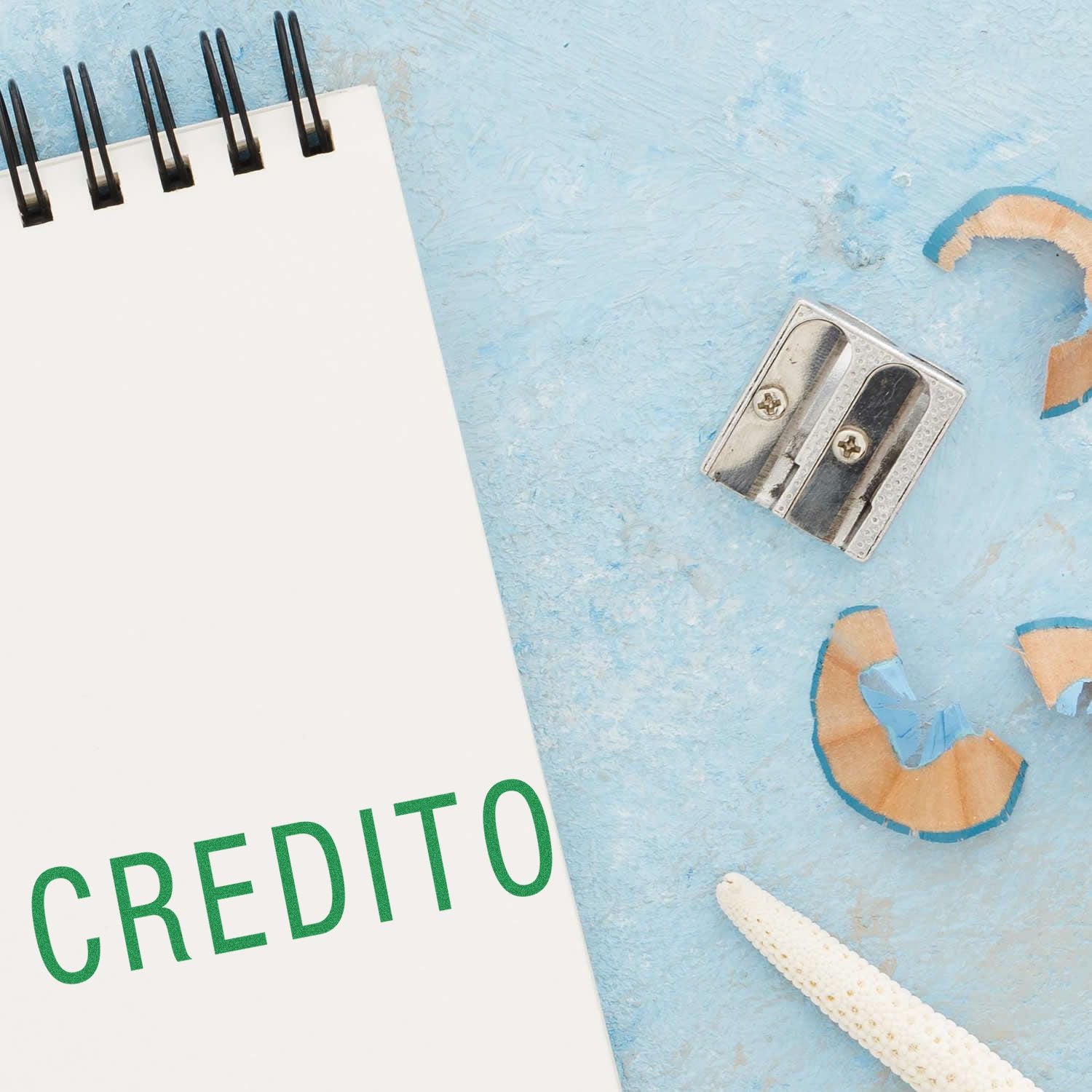 A Large Credito Rubber Stamp imprint on a white notepad, next to a pencil sharpener and shavings on a light blue surface.