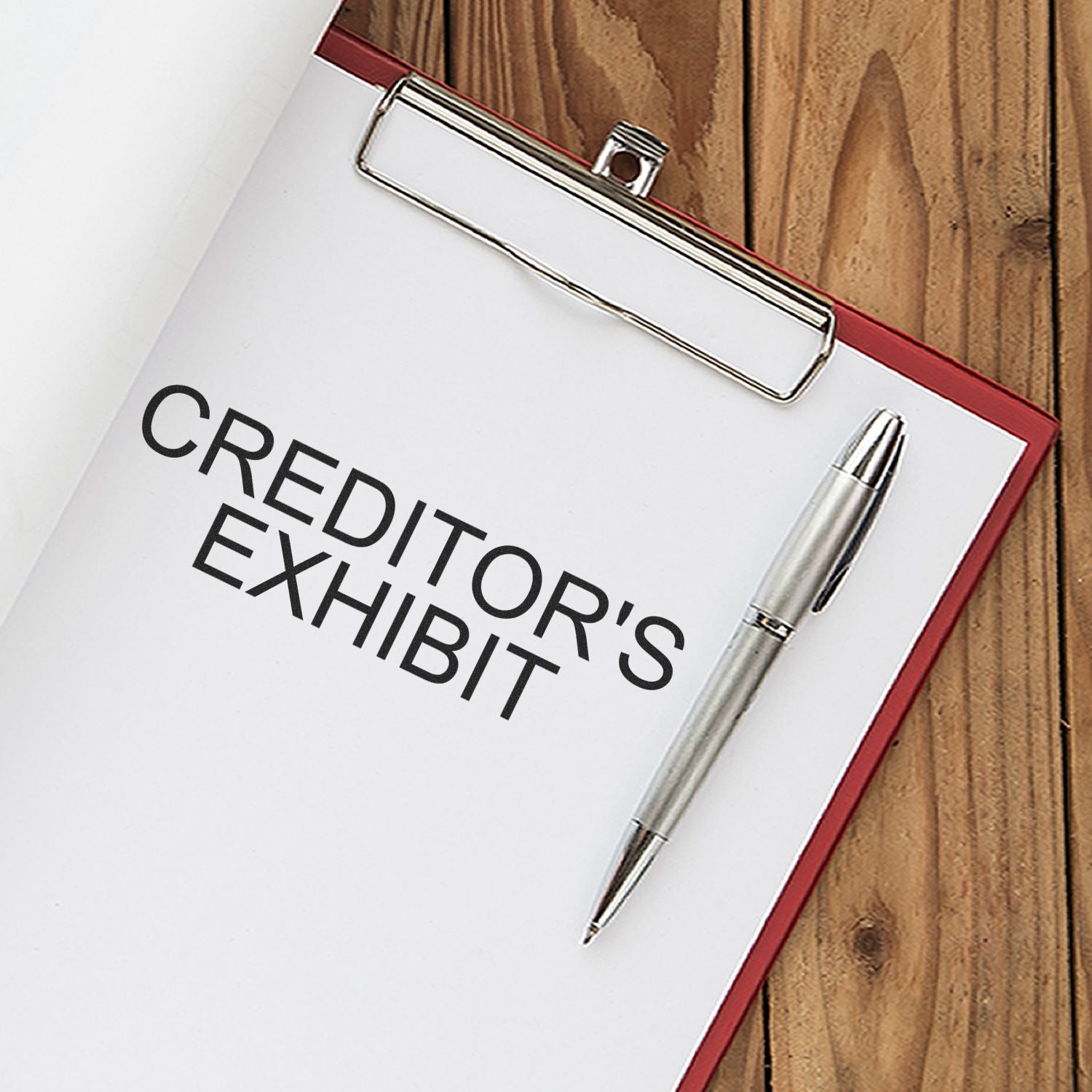 A clipboard with a paper stamped CREDITOR'S EXHIBIT using the Creditors Exhibit Rubber Stamp, alongside a silver pen on a wooden surface.