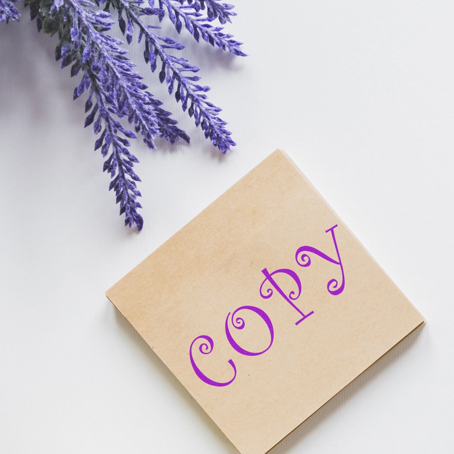 Curly Copy Rubber Stamp in use, stamping the word COPY in purple on a brown paper, with lavender flowers in the background.