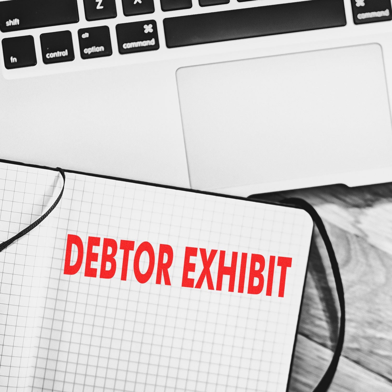 Notebook stamped with DEBTOR EXHIBIT in red ink using the Large Self Inking Debtor Exhibit Stamp, placed beside a laptop.