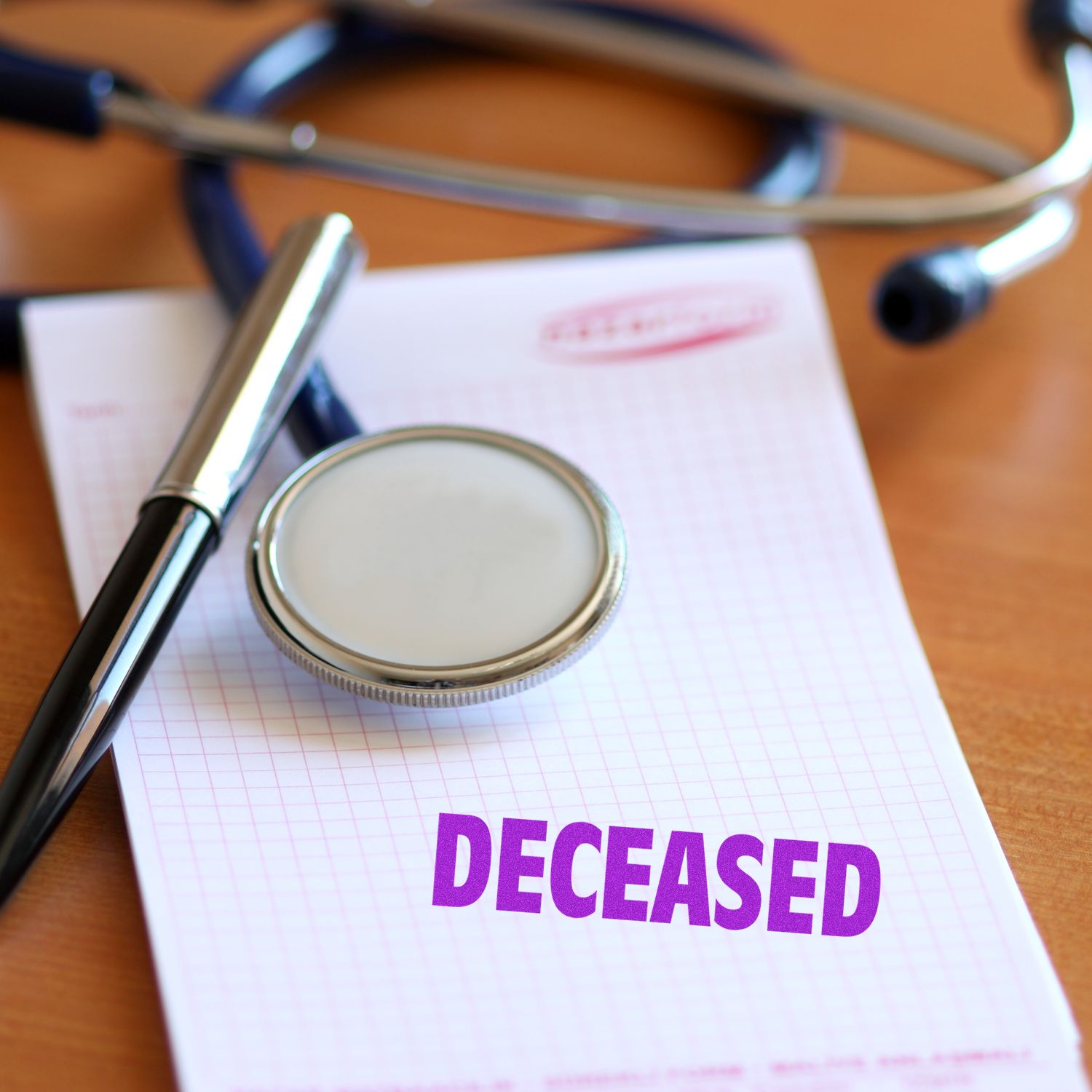 A stethoscope and pen on a notepad stamped with DECEASED using the Self Inking Deceased Stamp.