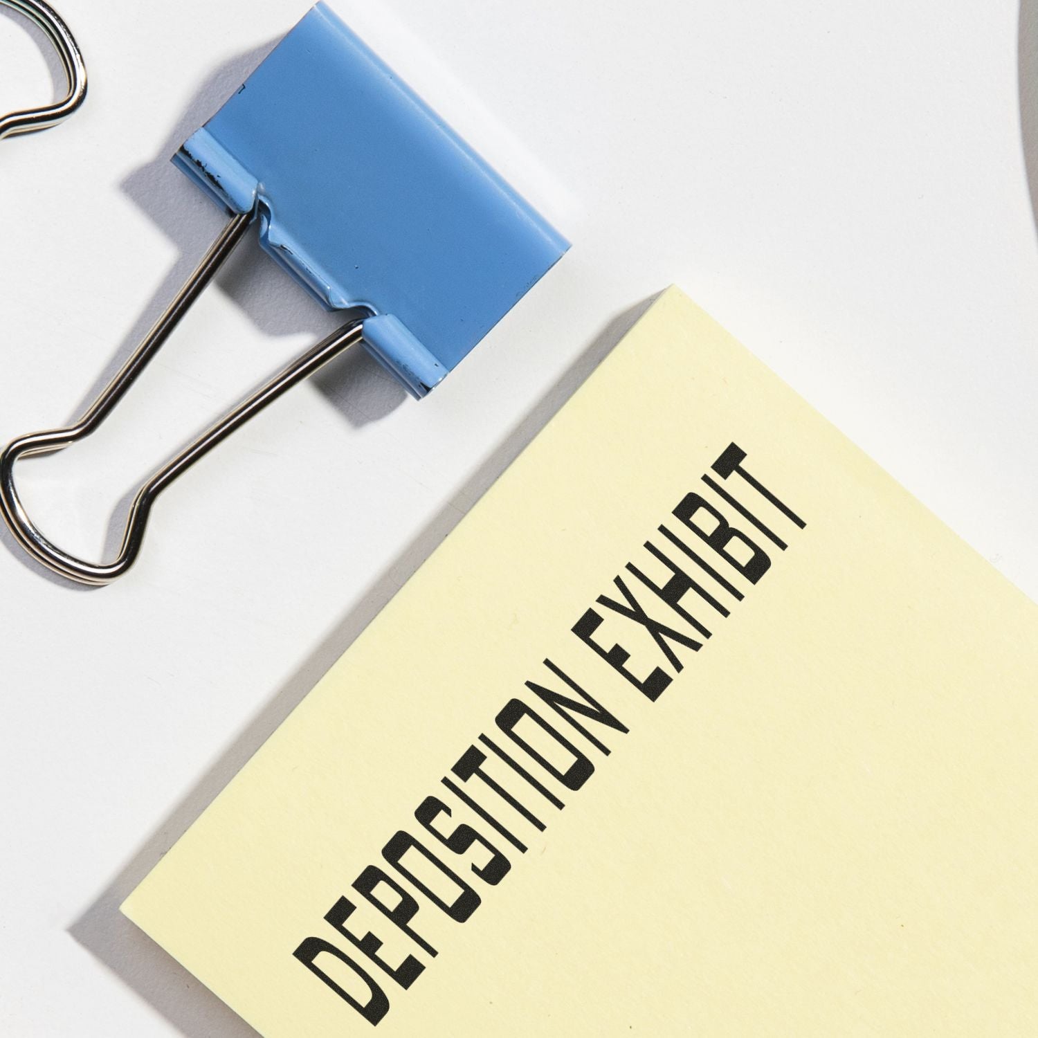 Large Self Inking Deposition Exhibit Stamp used on a yellow document next to a blue binder clip on a white surface.