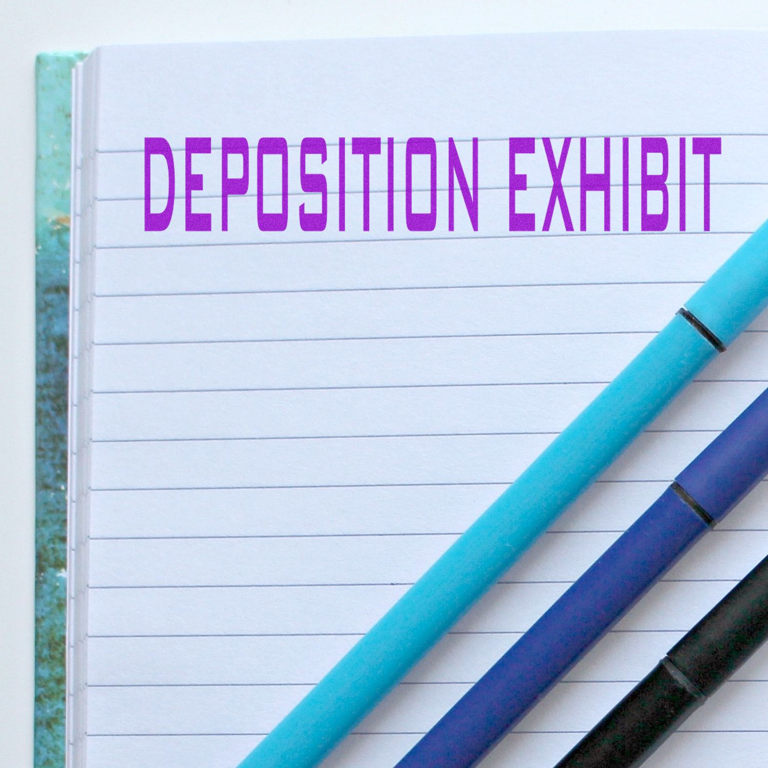 Large Deposition Exhibit Rubber Stamp imprint on a lined notebook page with three pens placed diagonally across the page.