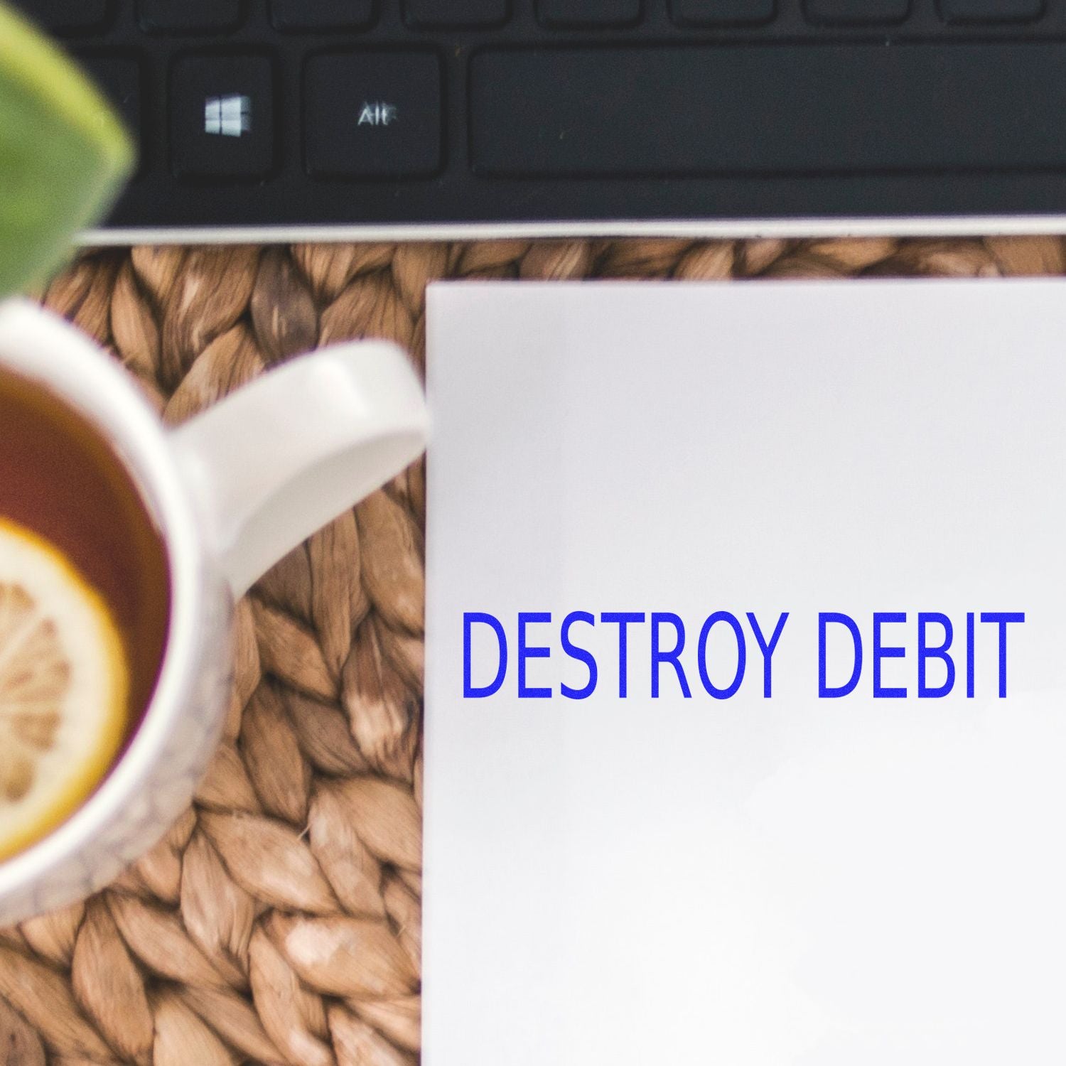 Destroy Debit Rubber Stamp in blue ink on white paper, next to a cup of tea with lemon and a keyboard in the background.