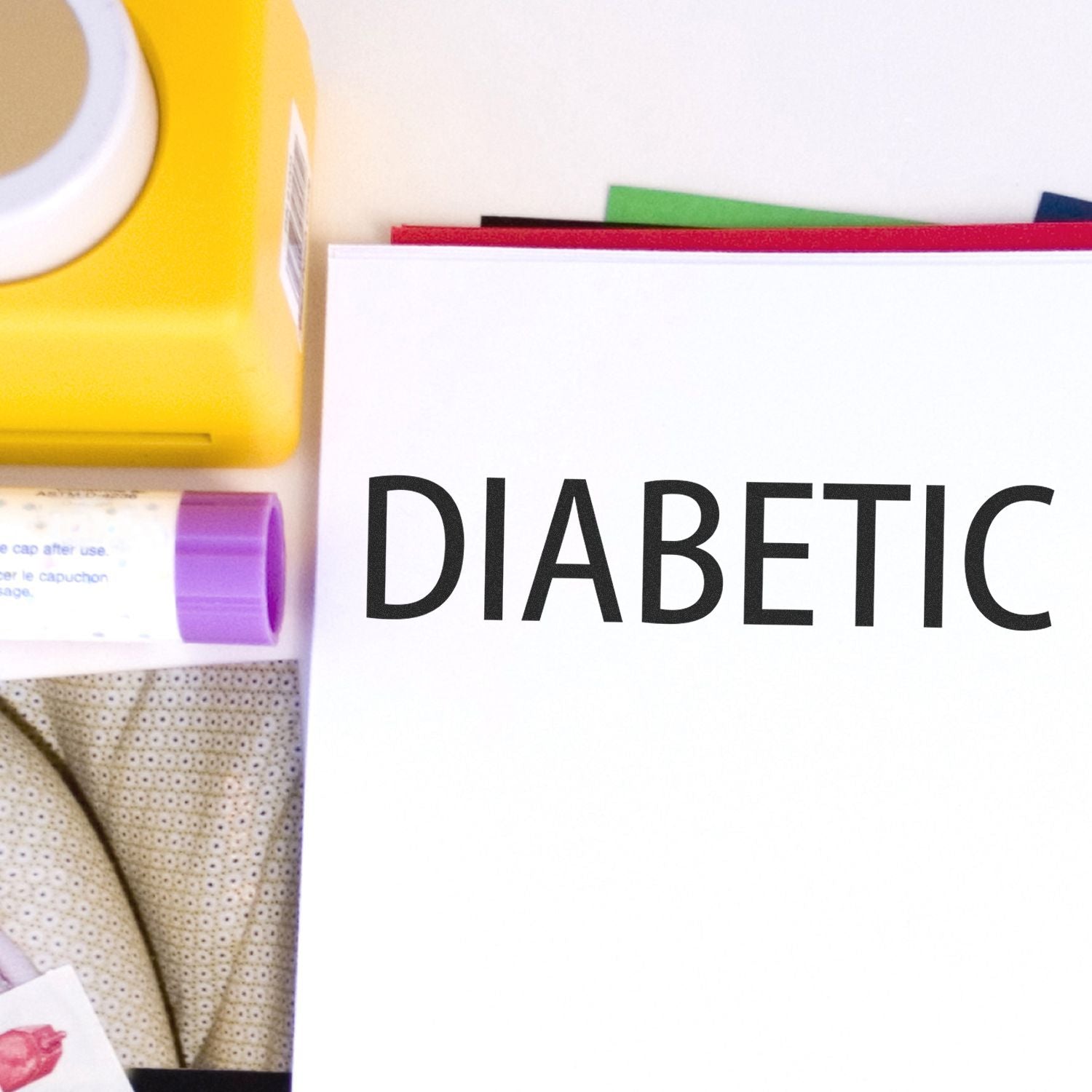 Diabetic Rubber Stamp in use, stamping the word DIABETIC on a white sheet, with a yellow stamp pad and other items in the background.