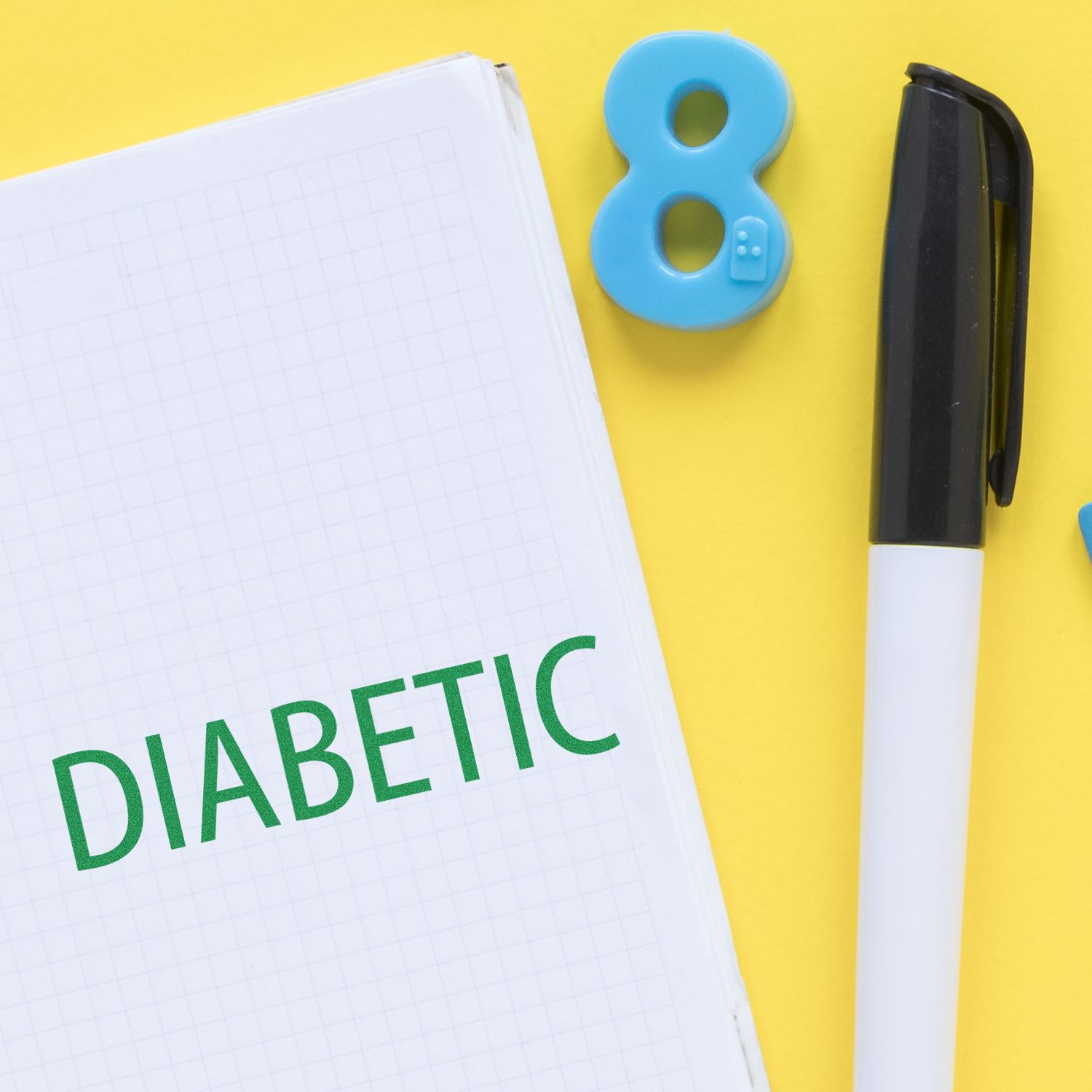 Large Self Inking Diabetic Stamp in use on a notebook with the word DIABETIC stamped, alongside a pen and blue number 8 on a yellow background.