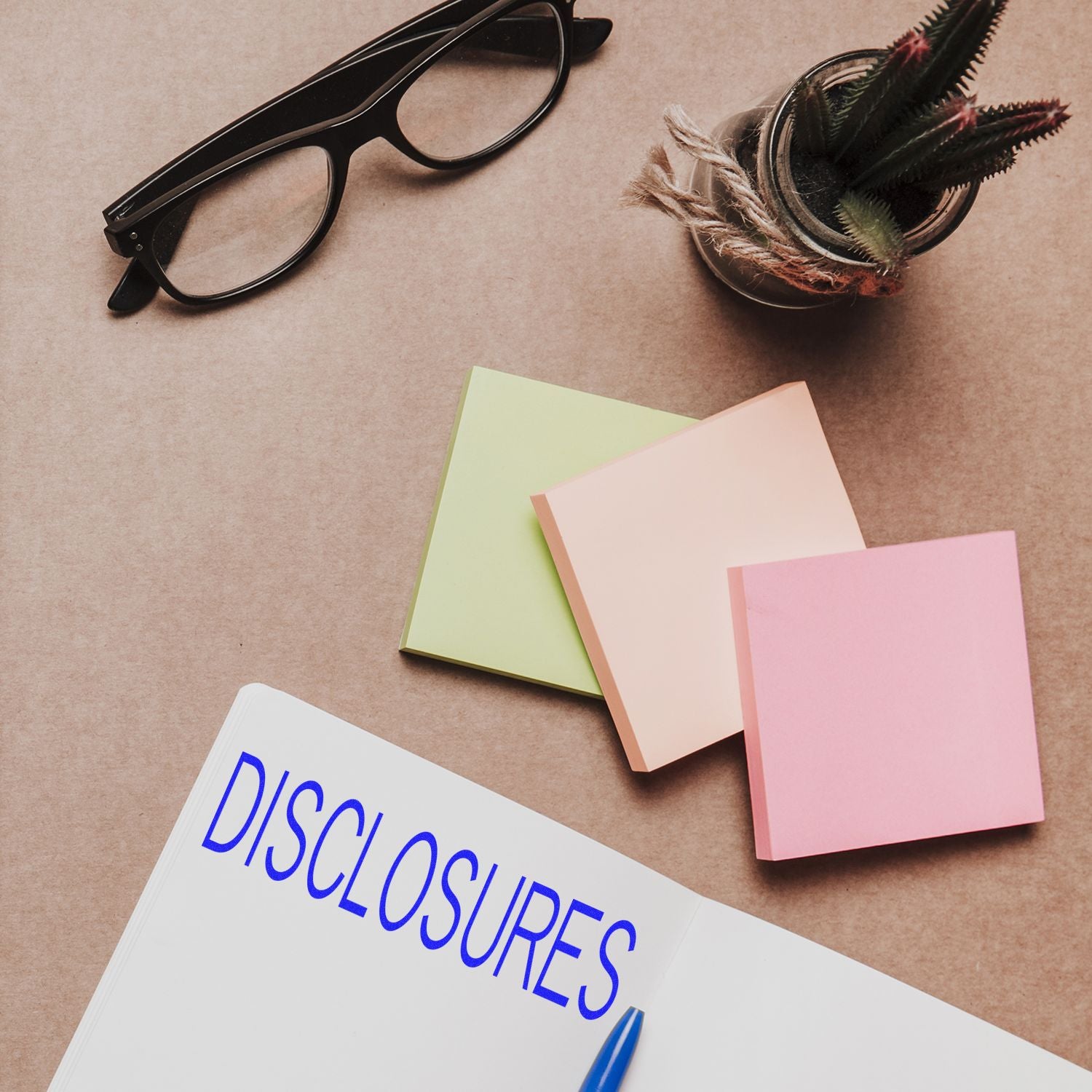 Self Inking Disclosures Stamp in use on a notebook, with sticky notes, glasses, and a potted plant on a desk.