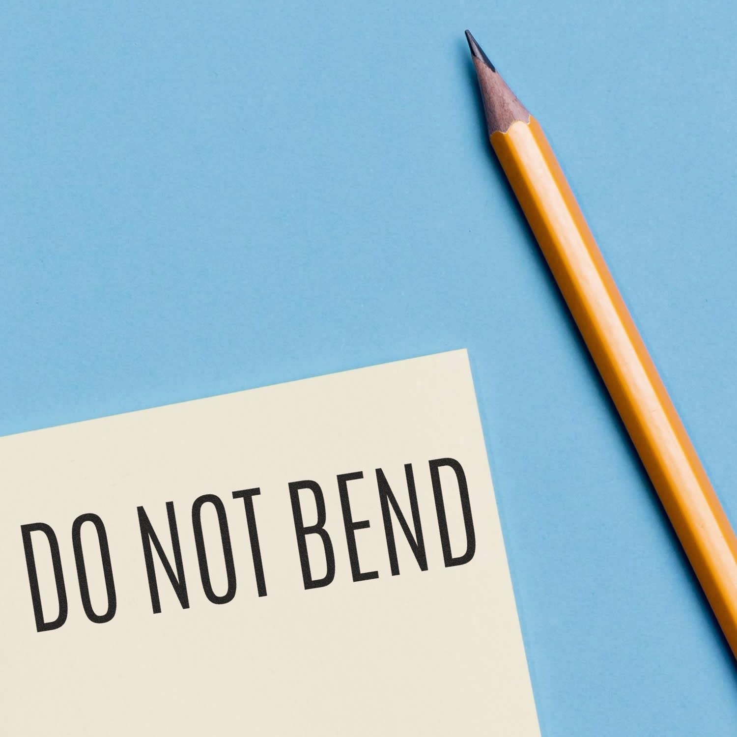 A yellow pencil next to a stamped paper with DO NOT BEND text using the Do Not Bend Rubber Stamp on a blue background.