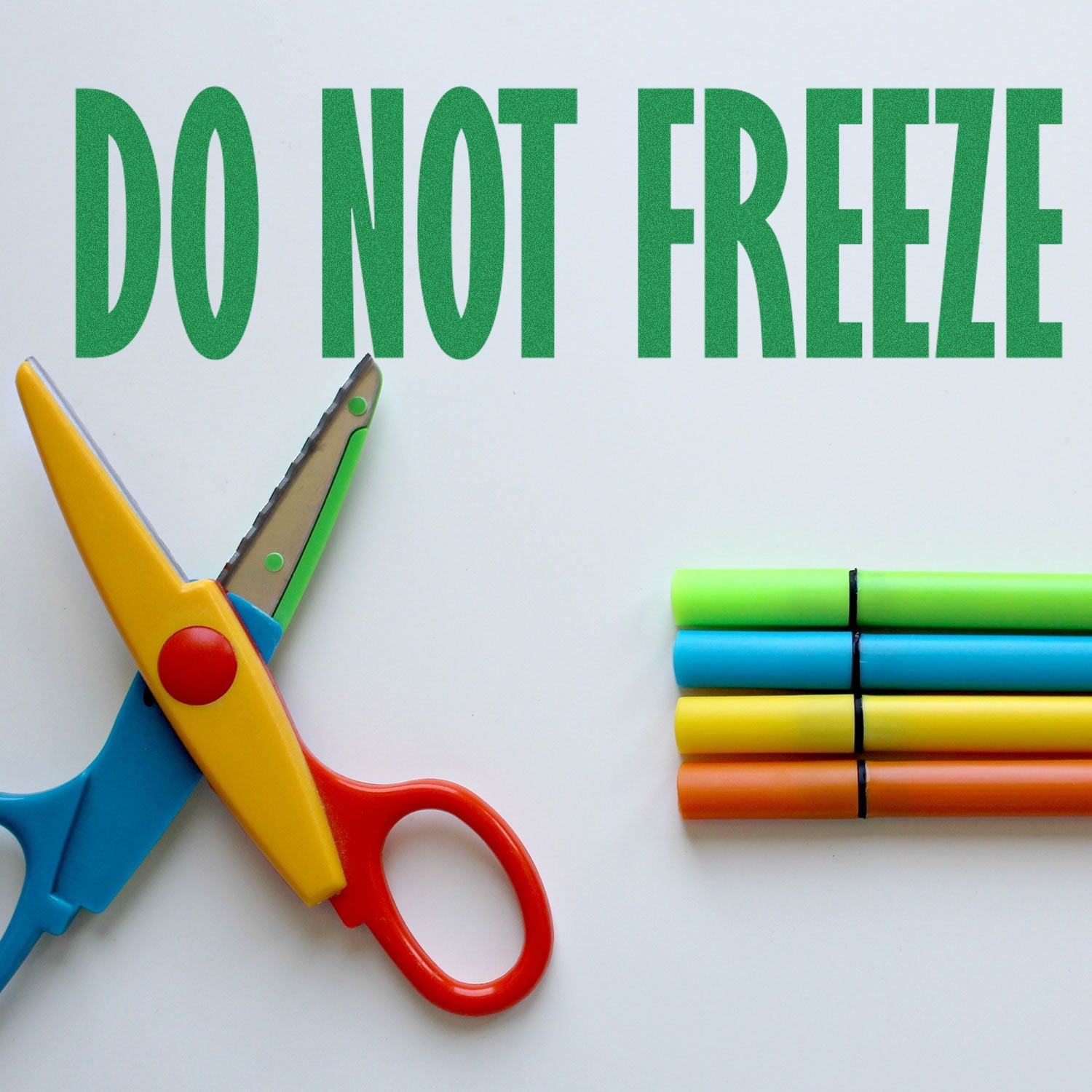 Colorful scissors and markers next to a Do Not Freeze Rubber Stamp imprint on a white surface.