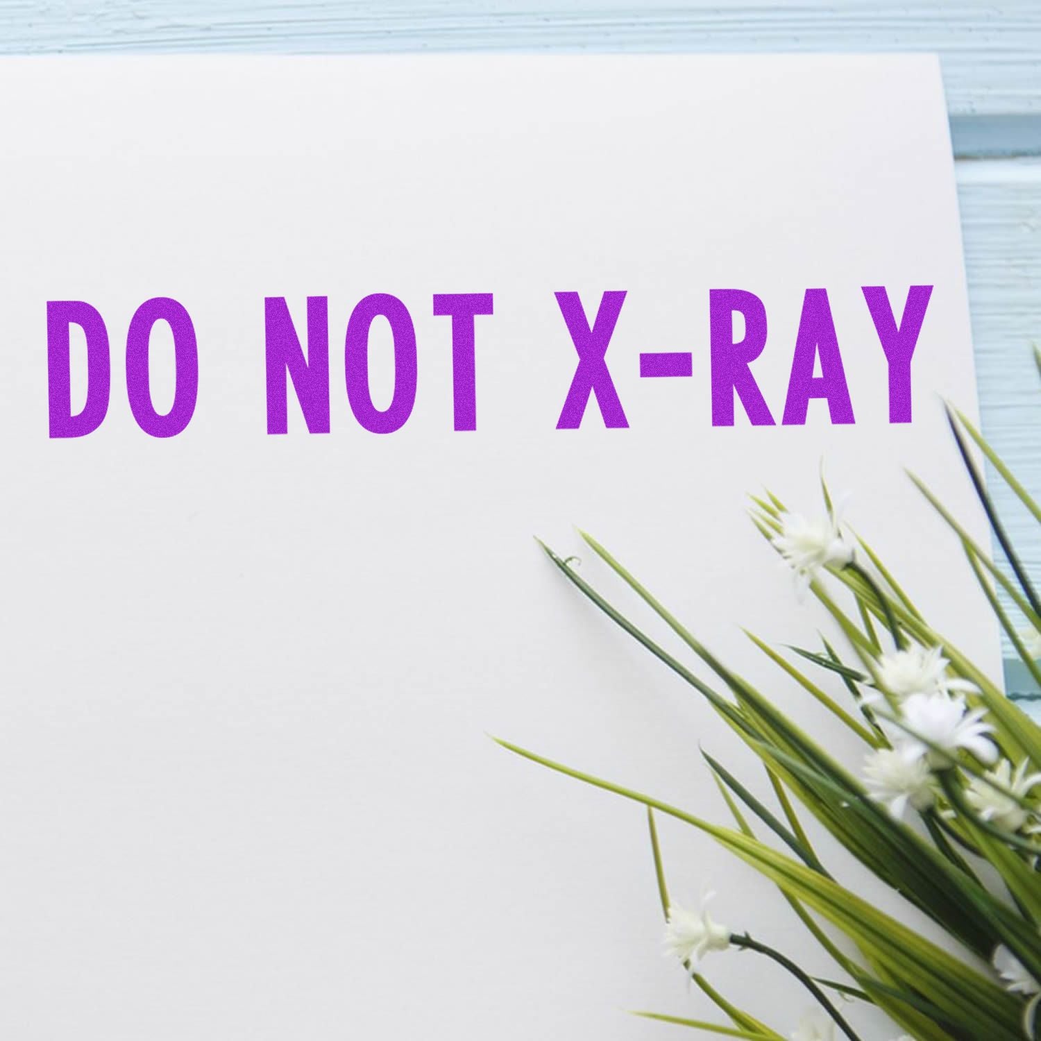 Do Not X-Ray Rubber Stamp imprint in purple ink on white paper, with green and white flowers on the side.