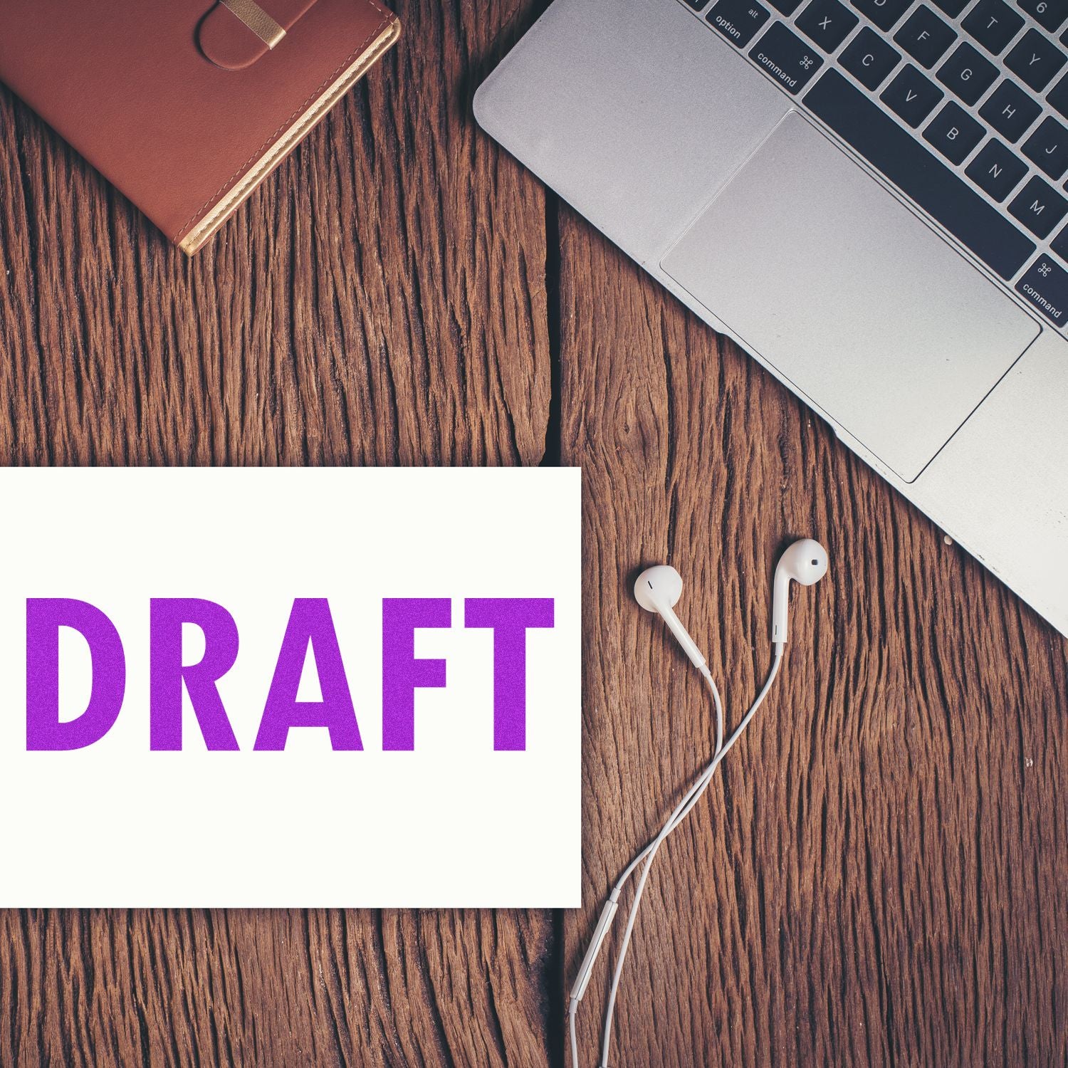 Slim Pre-Inked Draft Stamp in purple on paper, next to a laptop, earphones, and a brown notebook on a wooden desk.