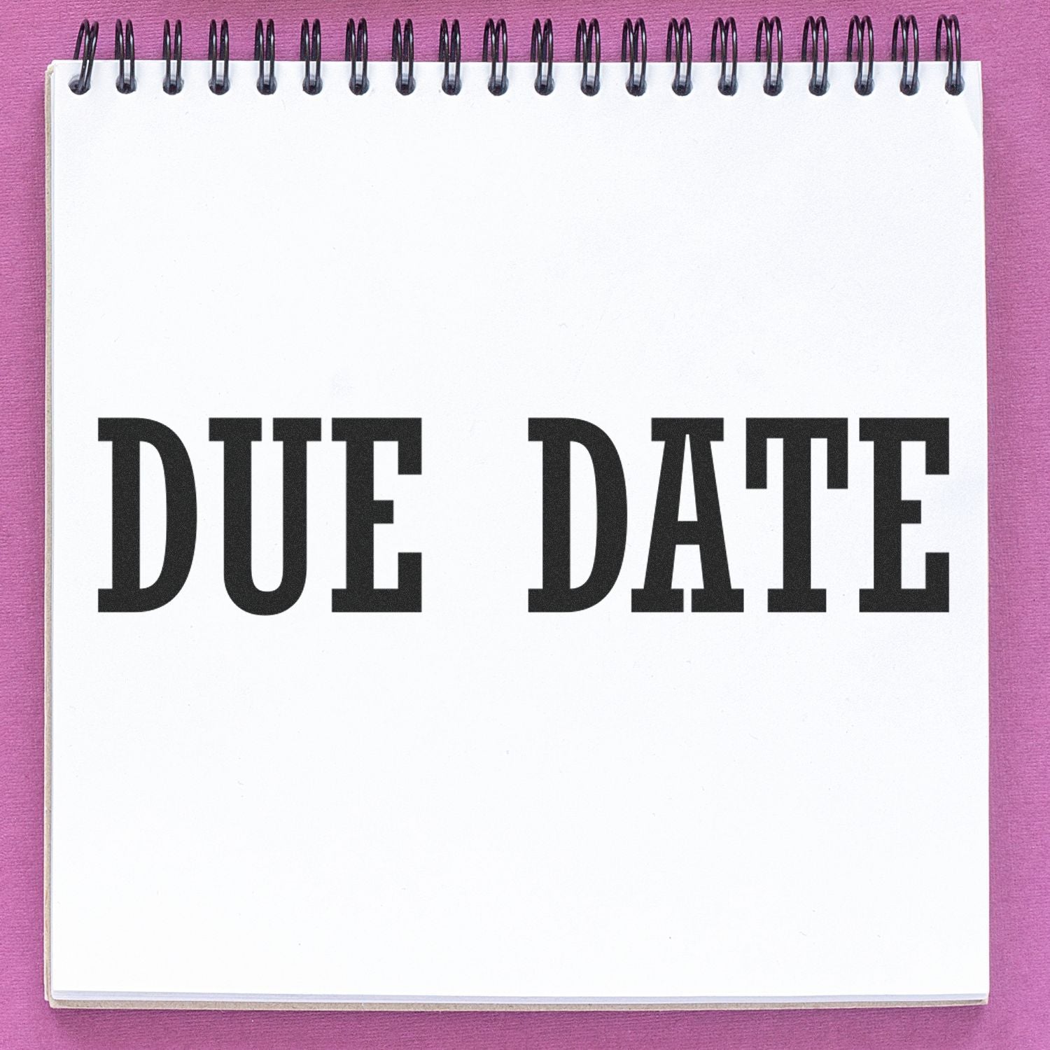 A notebook with DUE DATE stamped on a page using the Due Date Rubber Stamp, placed on a pink surface.