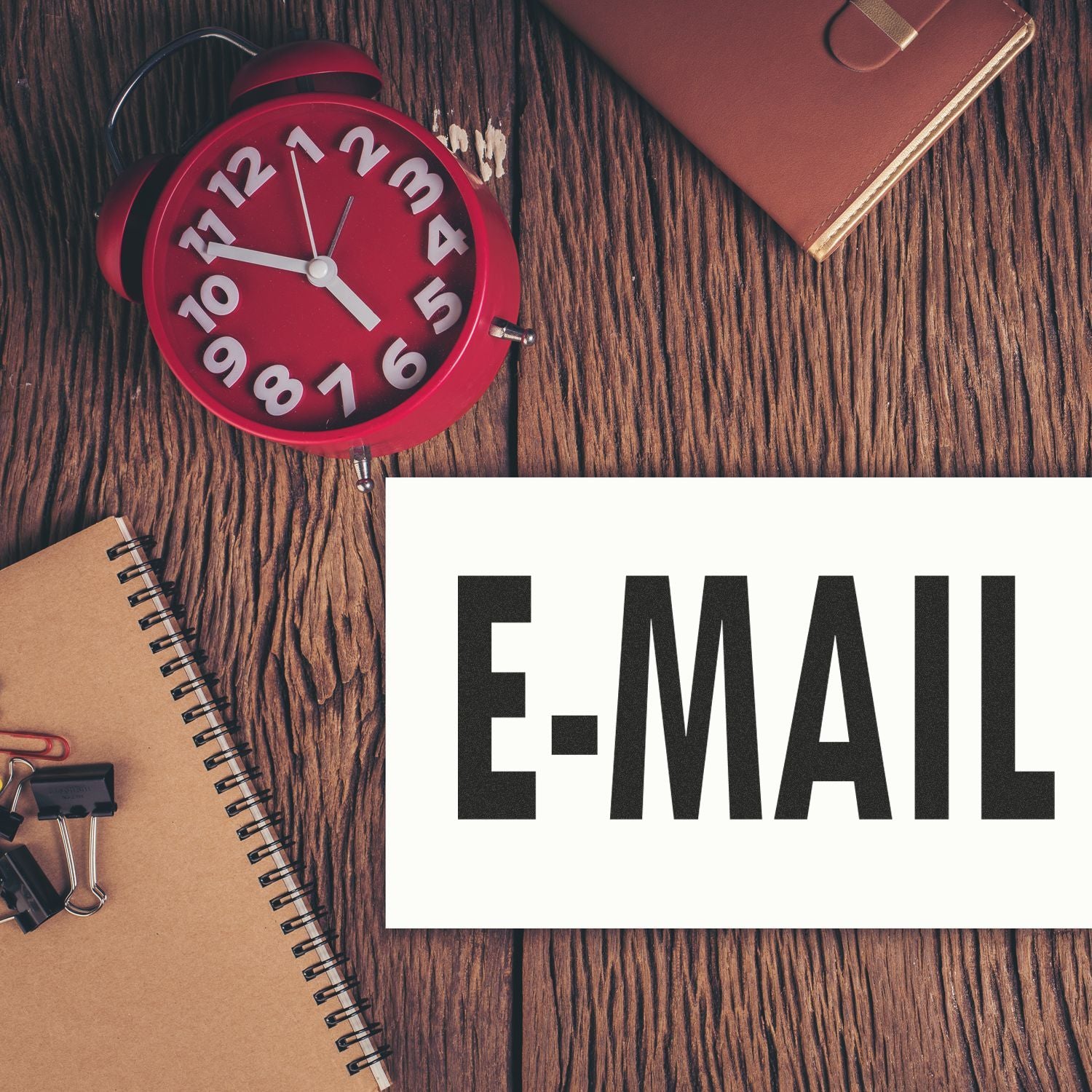 Large E Mail Rubber Stamp used on a white card, placed on a wooden desk with a red clock, notebook, and office supplies.