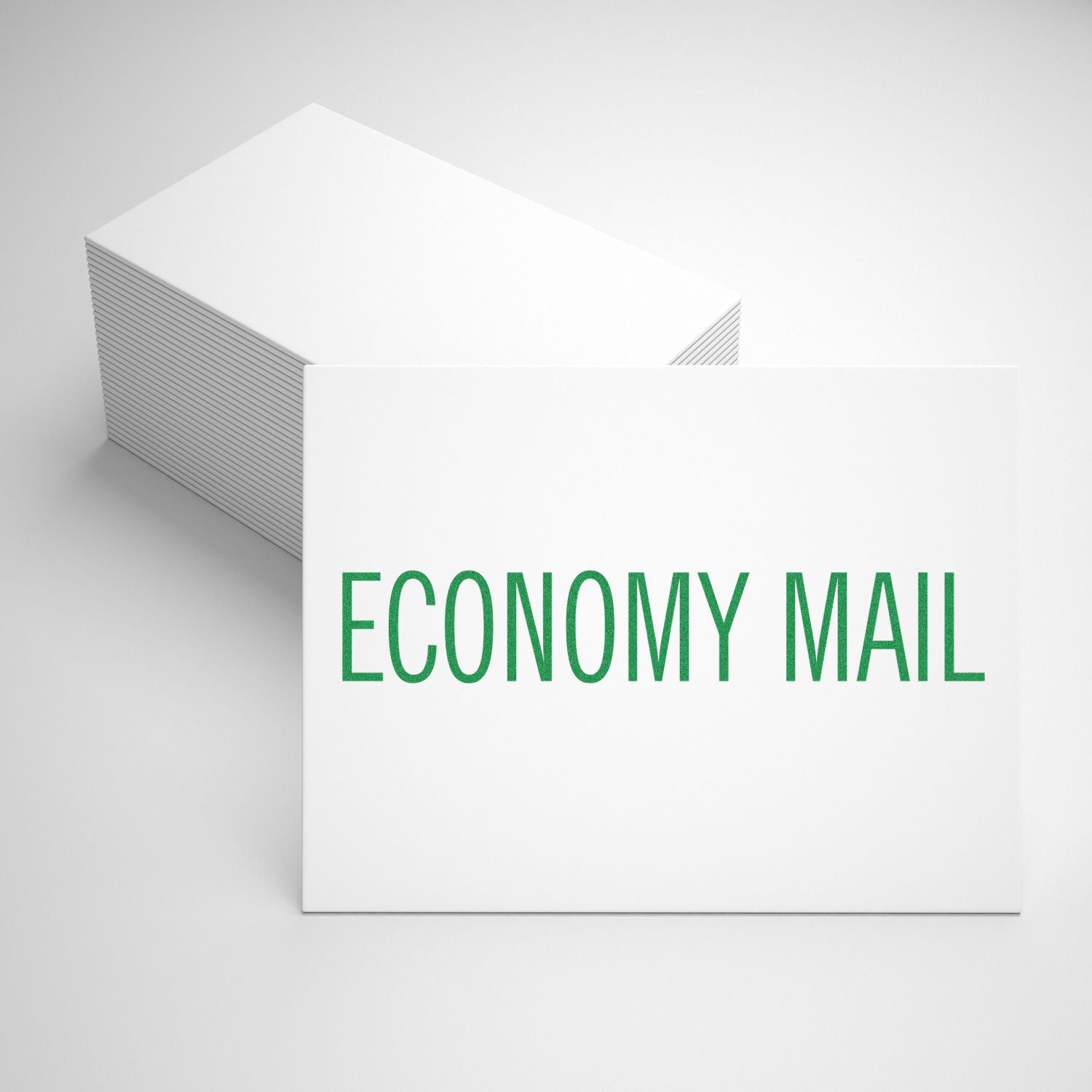 Stack of white cards stamped with ECONOMY MAIL in green using a Slim Pre-Inked Economy Mail Stamp, placed on a white surface.