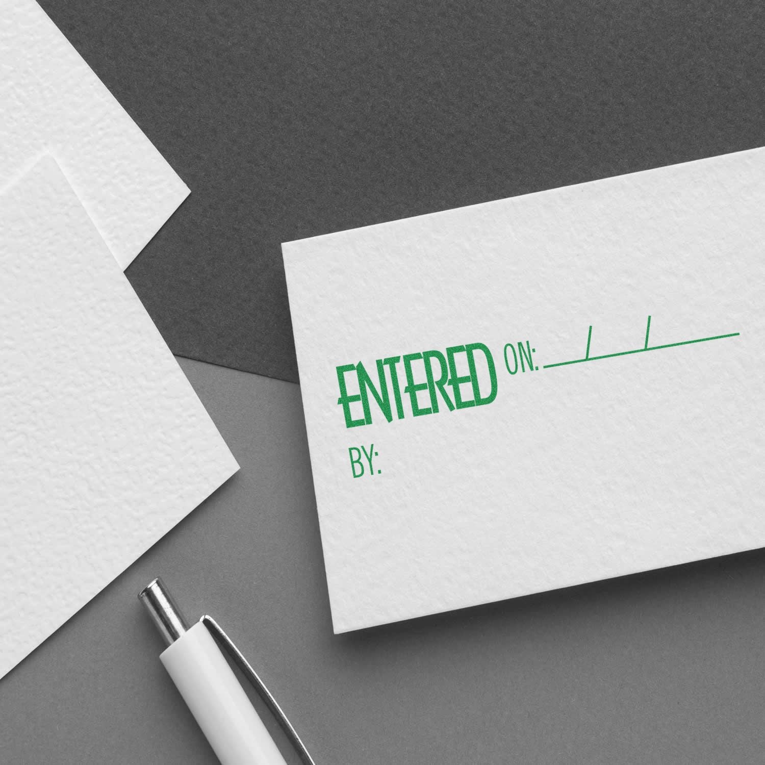 Large Entered On Rubber Stamp in green ink on a white card with spaces for date and signature, placed on a gray surface with a pen nearby.