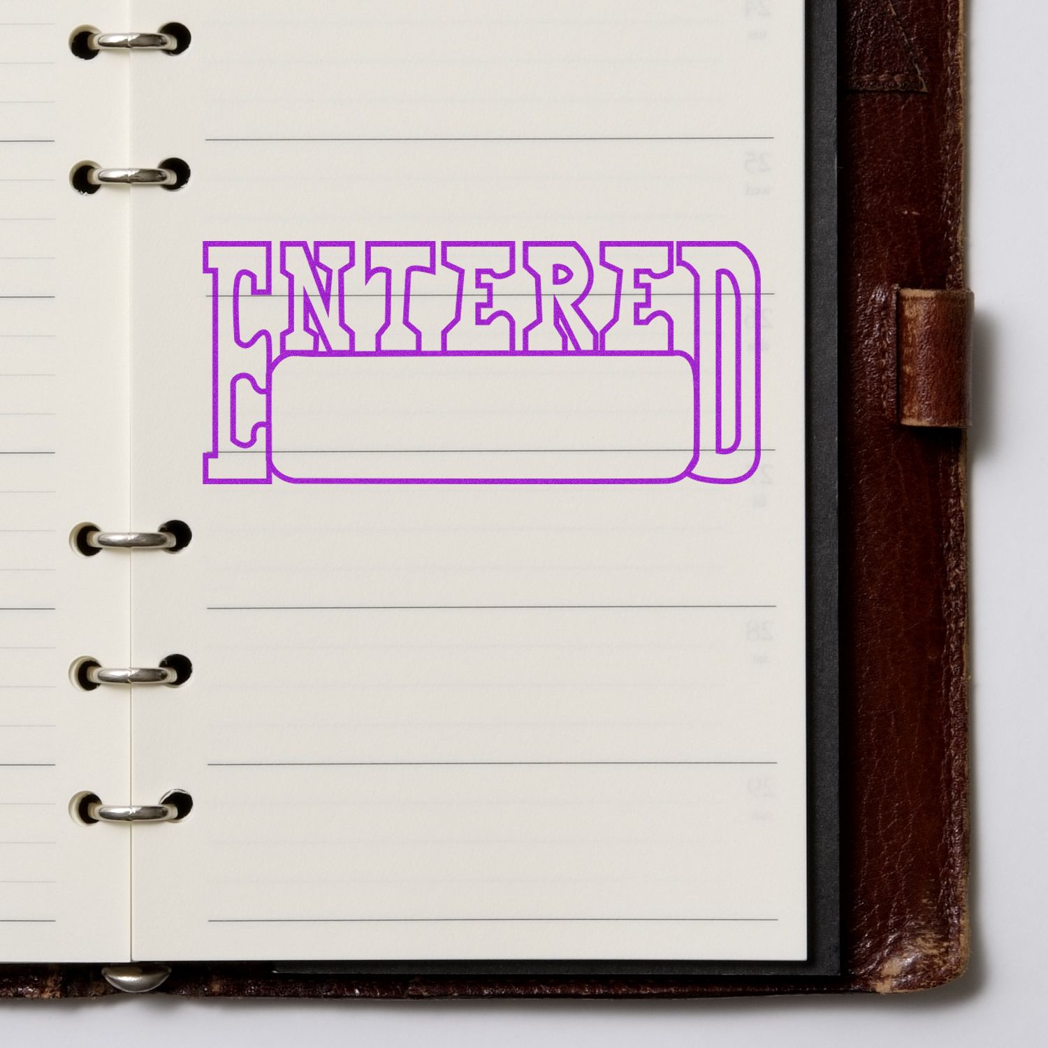 Large Entered with Date Box Rubber Stamp in purple ink on an open notebook with lined pages and a brown leather cover.