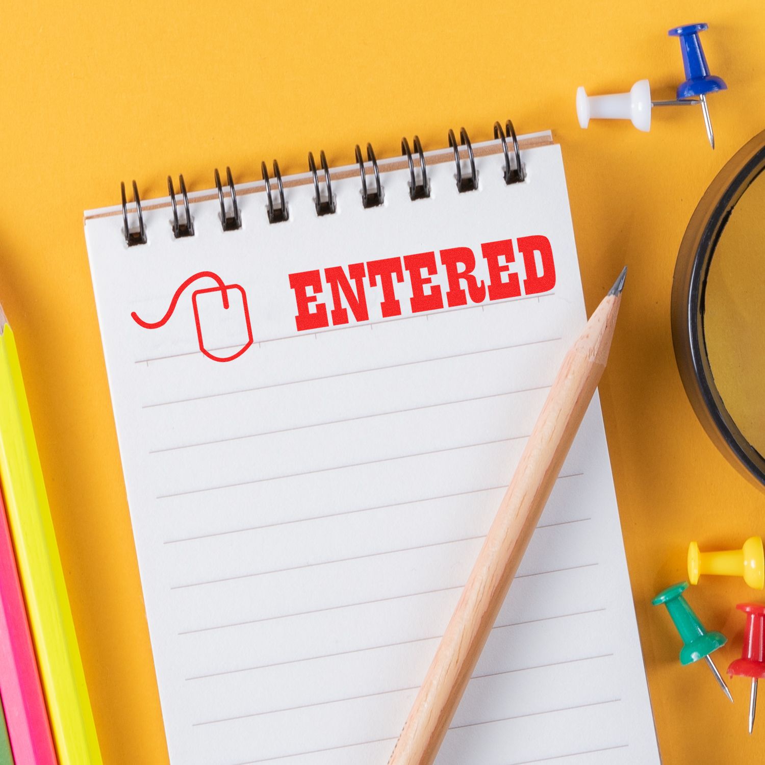 A notepad stamped with Entered using the Entered with Mouse Rubber Stamp, surrounded by colorful pencils, push pins, and a magnifying glass.