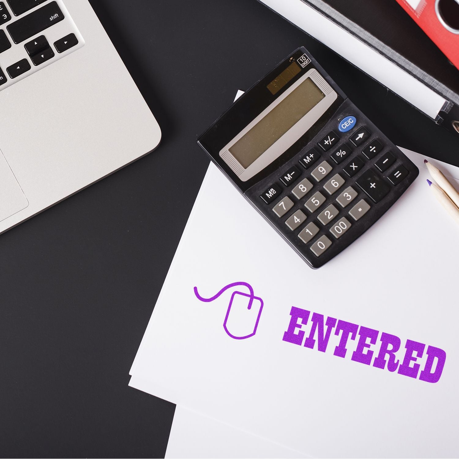 Calculator on papers stamped with Entered with Mouse Rubber Stamp in purple ink, next to a laptop and a pencil on a black desk.