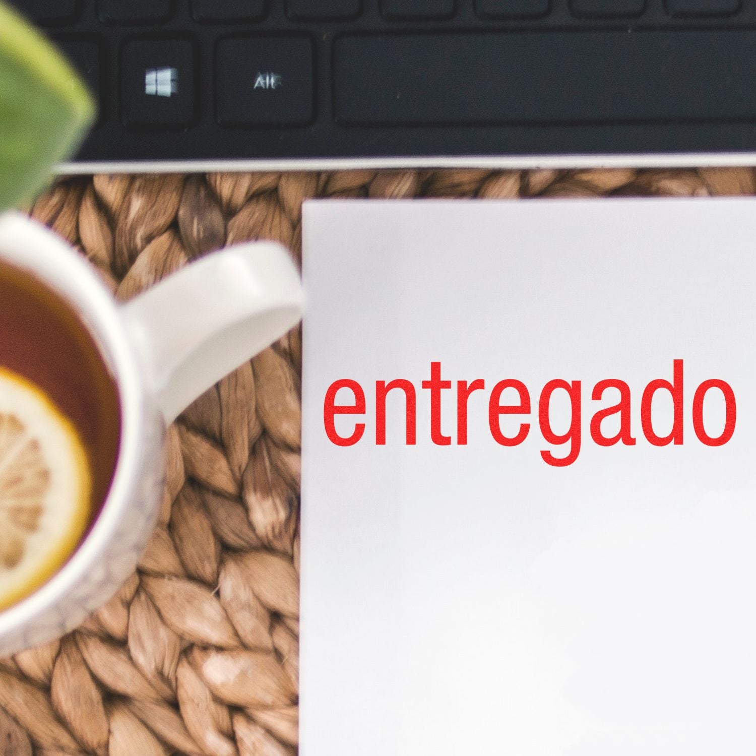 Large Entregado Rubber Stamp used on white paper, next to a keyboard and a cup of tea with a lemon slice on a woven mat.