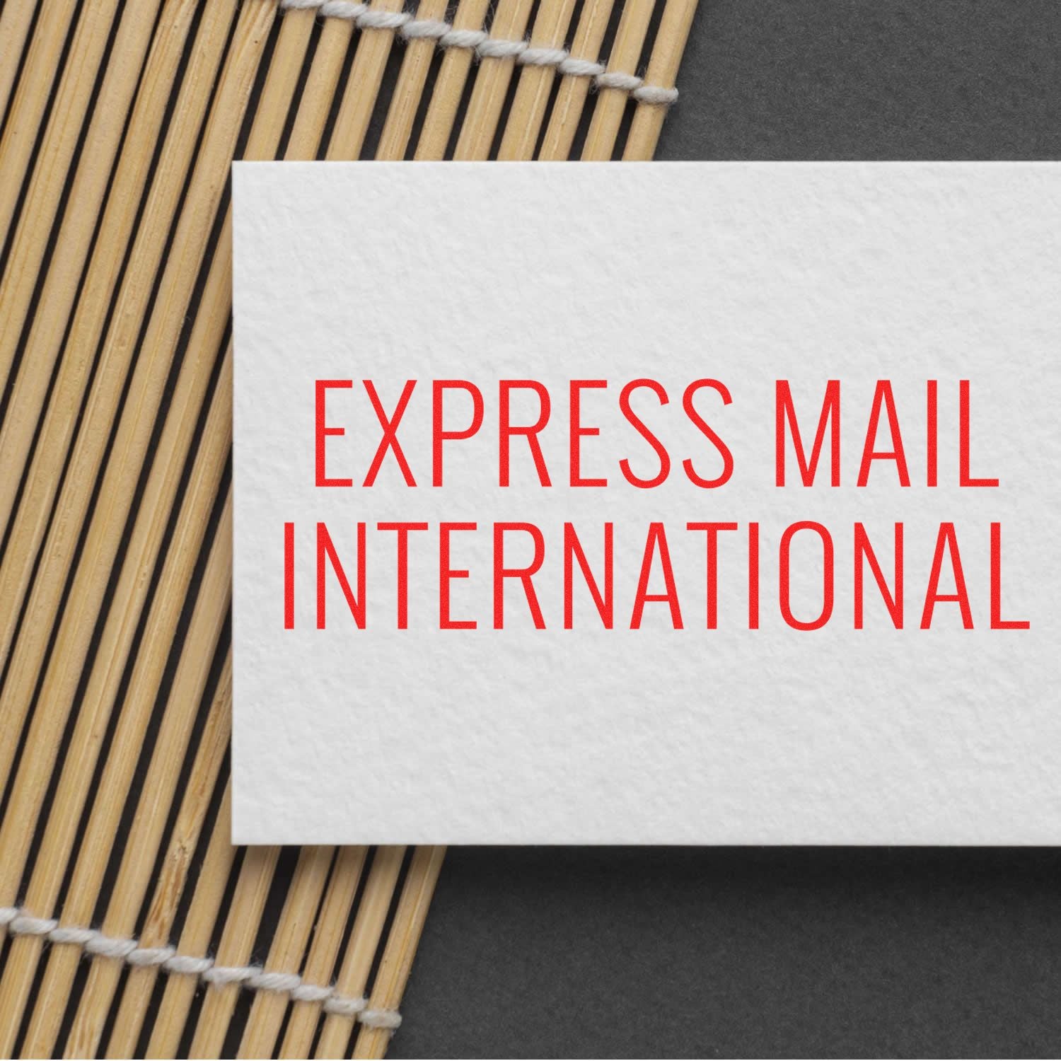 Express Mail International Rubber Stamp in red ink on a white card, placed on a bamboo mat and dark background.