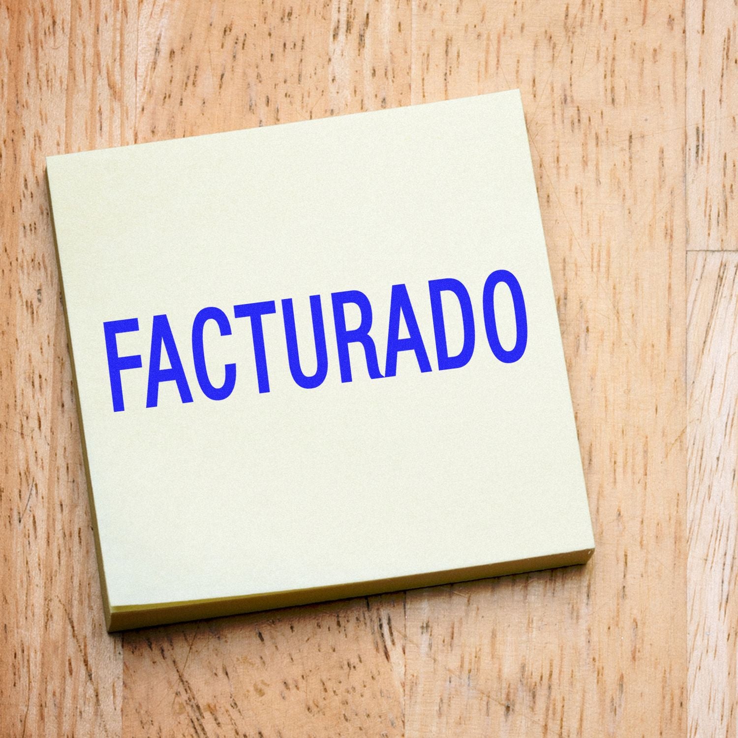 Facturado Rubber Stamp in use, displaying the word FACTURADO in bold blue letters on a light-colored paper, placed on a wooden surface.