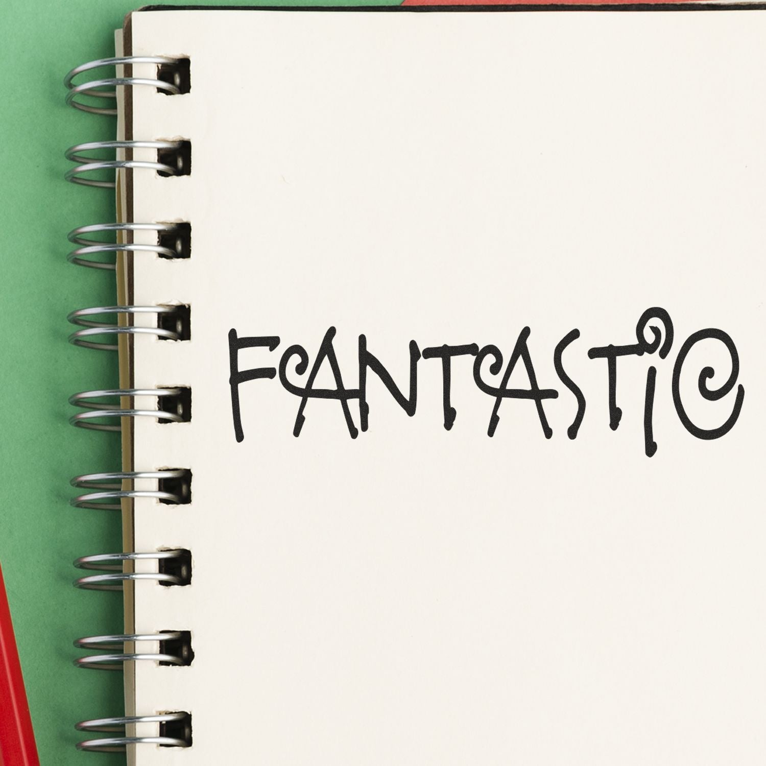 A spiral notebook with the word FANTASTIC stamped on a page using the Fantastic Rubber Stamp, placed on a green and red background.