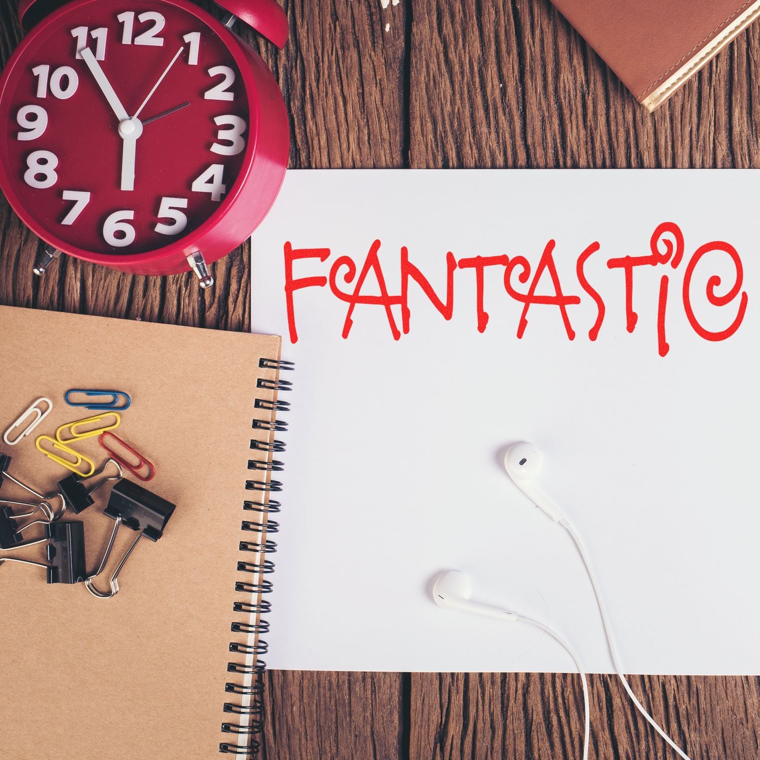 Desk with a red clock, notebook, paper clips, and a paper stamped with 'FANTASTIC' using a Slim Pre-Inked Fantastic Stamp.