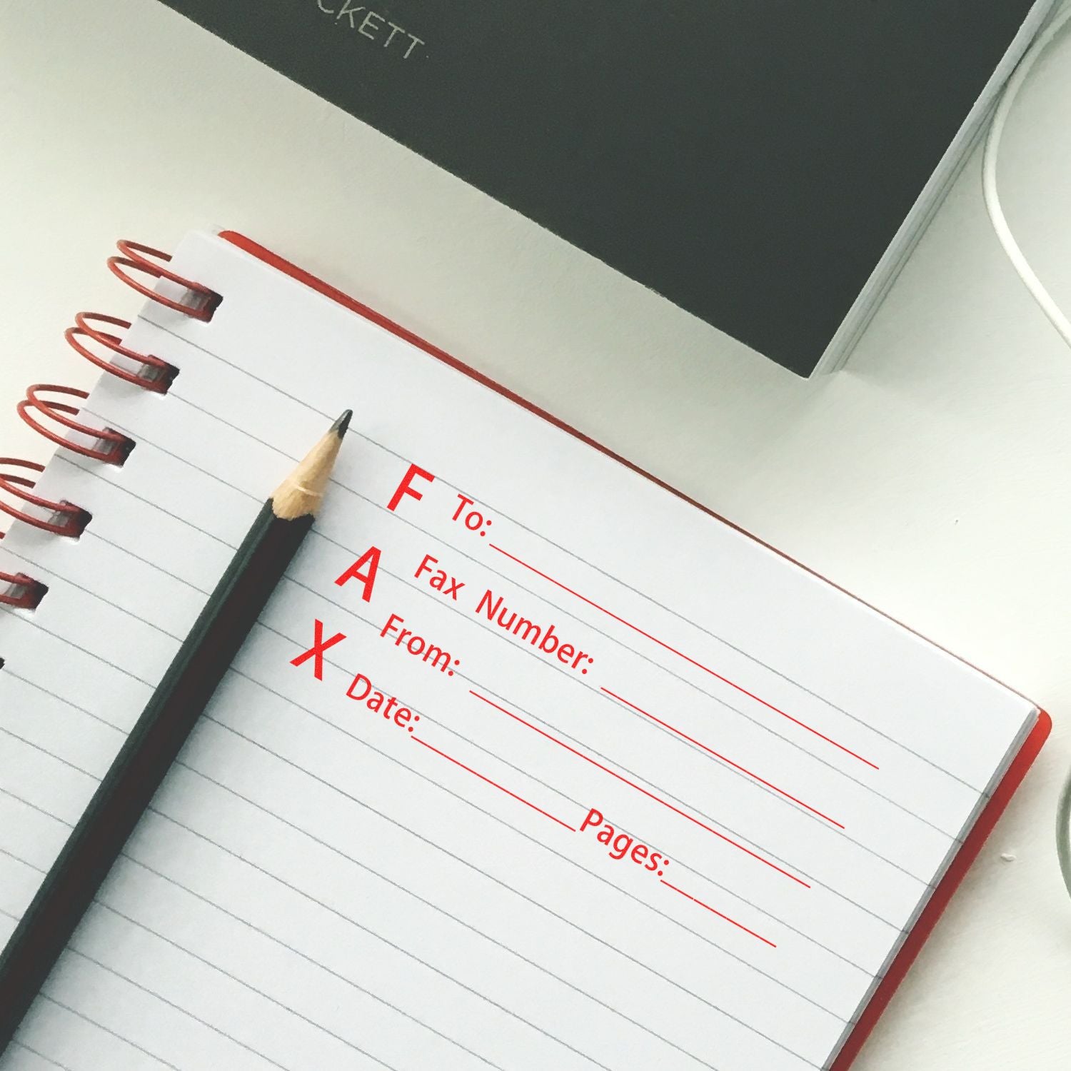 Notebook with FAX form stamped using Slim Pre-Inked Fax It 1 Stamp in red ink, next to a pencil on a white desk.