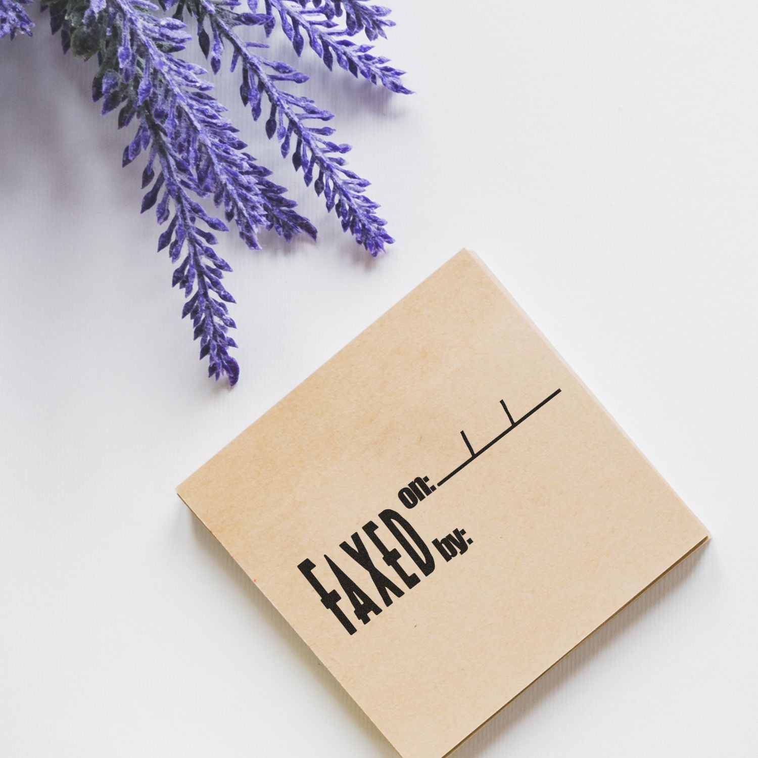 Large Self Inking Faxed on Stamp used on a brown envelope, placed on a white surface next to purple lavender flowers.