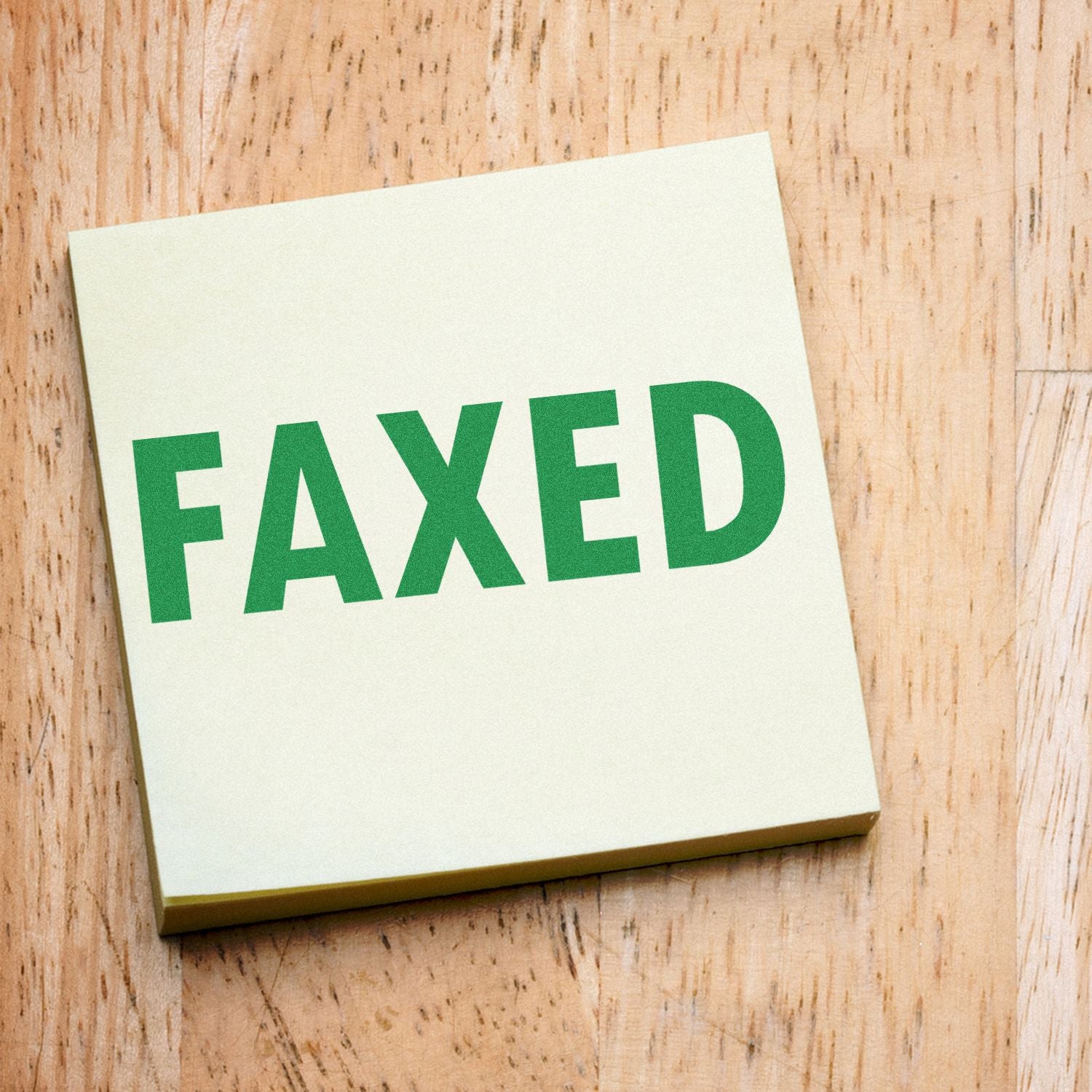 Large Self Inking Faxed Stamp in use, showing a green FAXED imprint on a yellow paper, placed on a wooden surface.