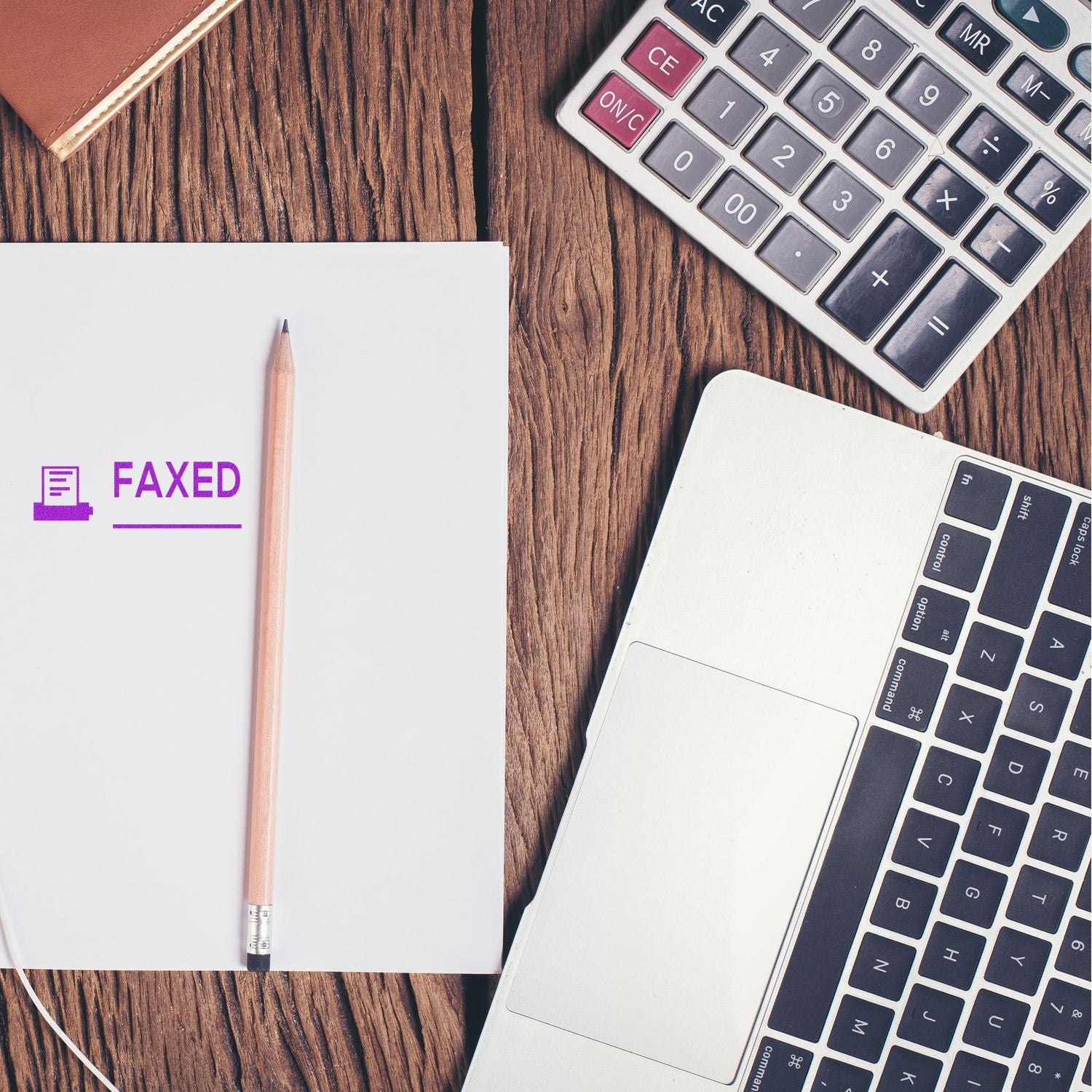 A desk with a laptop, calculator, notebook, pencil, and a paper stamped with Faxed with Machine Rubber Stamp in purple ink.