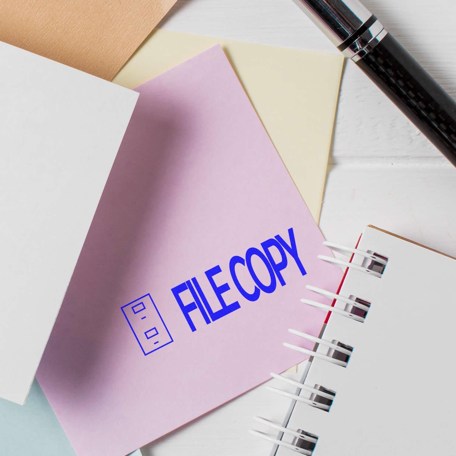 Self Inking File Copy with Drawer Stamp used on a pink document, surrounded by papers, a pen, and a notebook on a white surface.