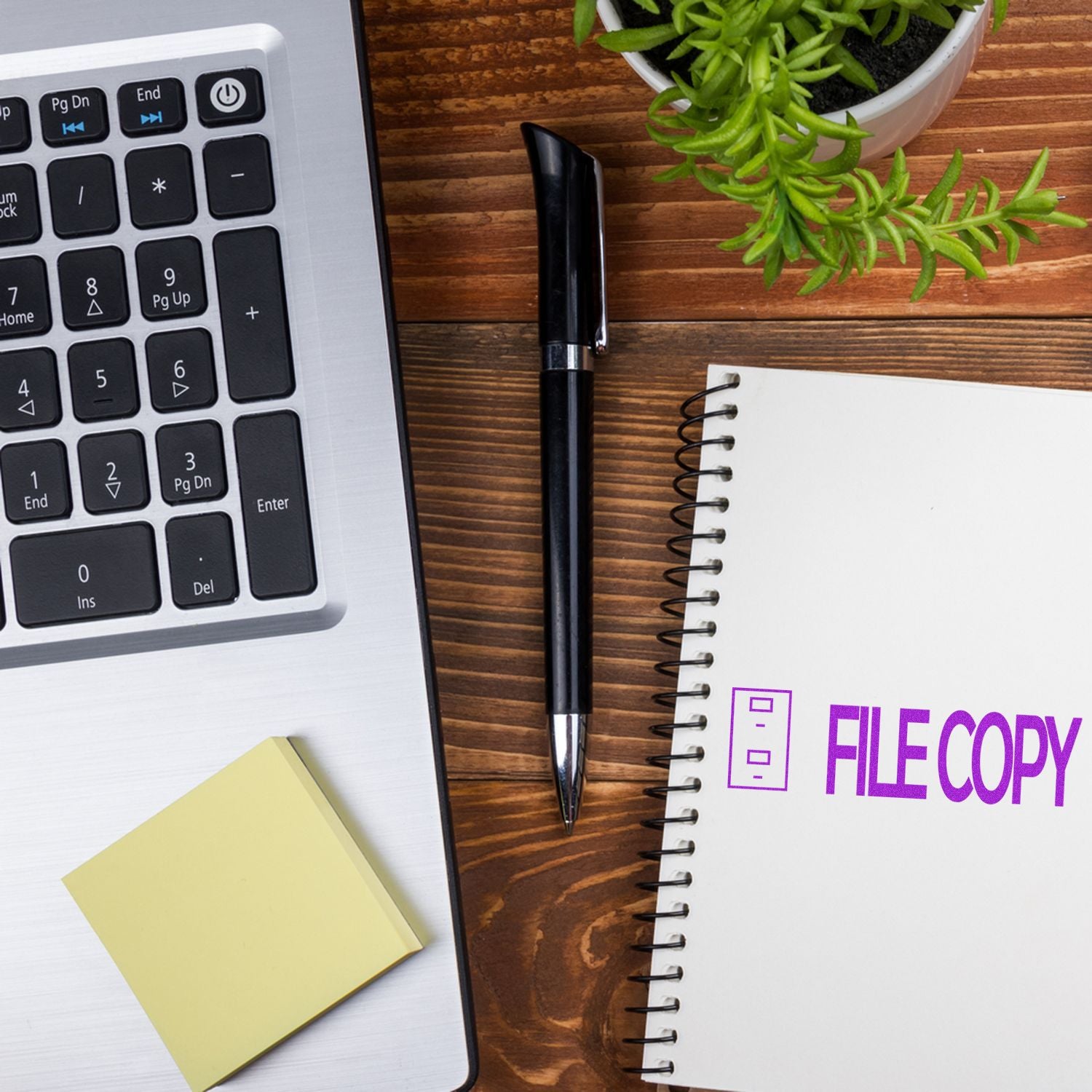 A laptop, pen, sticky notes, and a notebook stamped with File Copy with Drawer Rubber Stamp on a wooden desk with a small plant.