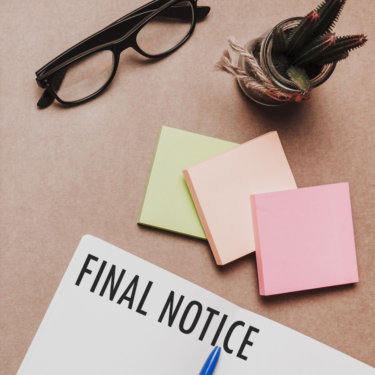 Large Self Inking Final Notice Stamp on paper, surrounded by sticky notes, glasses, and a small plant on a desk.