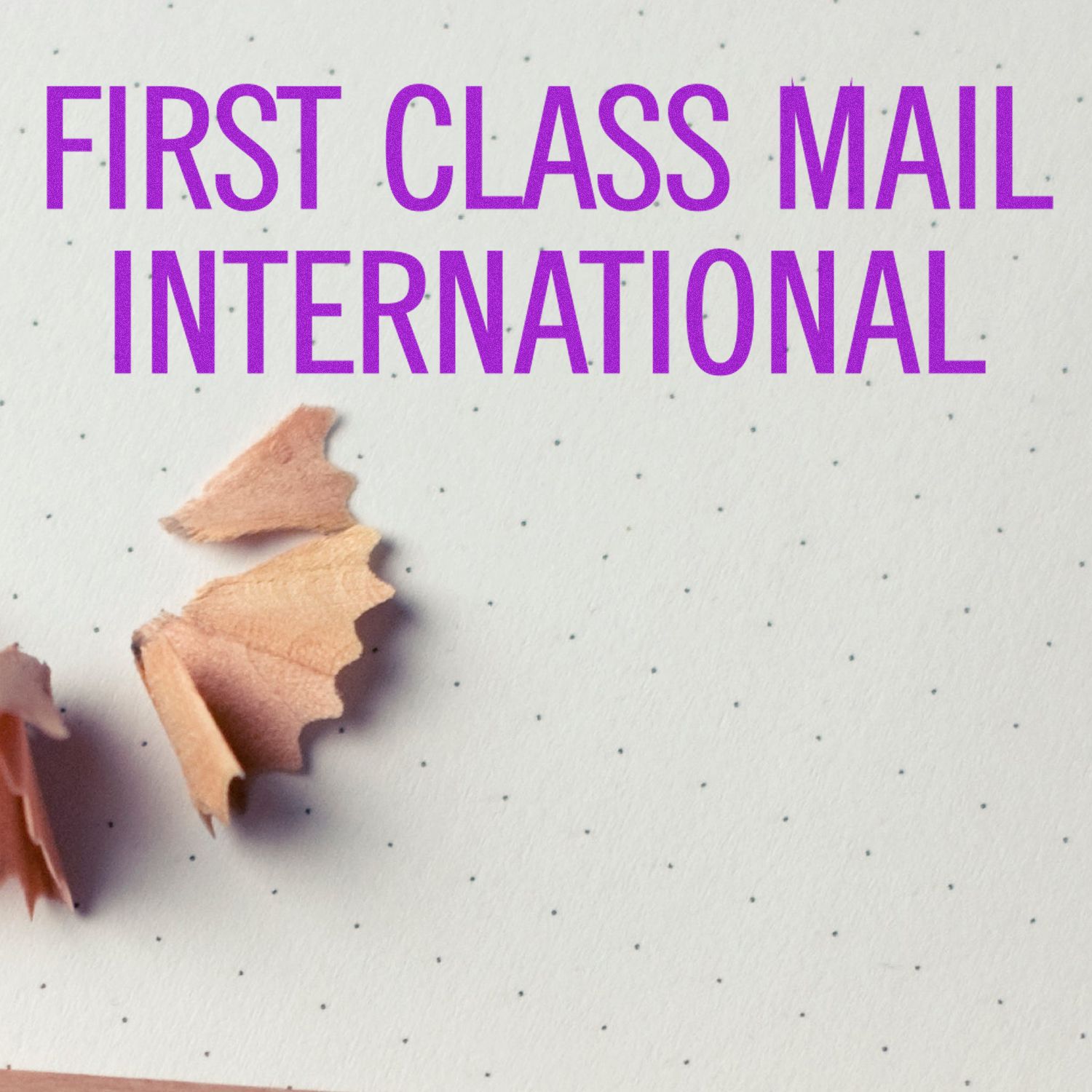 Large Self Inking First Class Mail International Stamp in use on dotted paper with pencil shavings nearby.