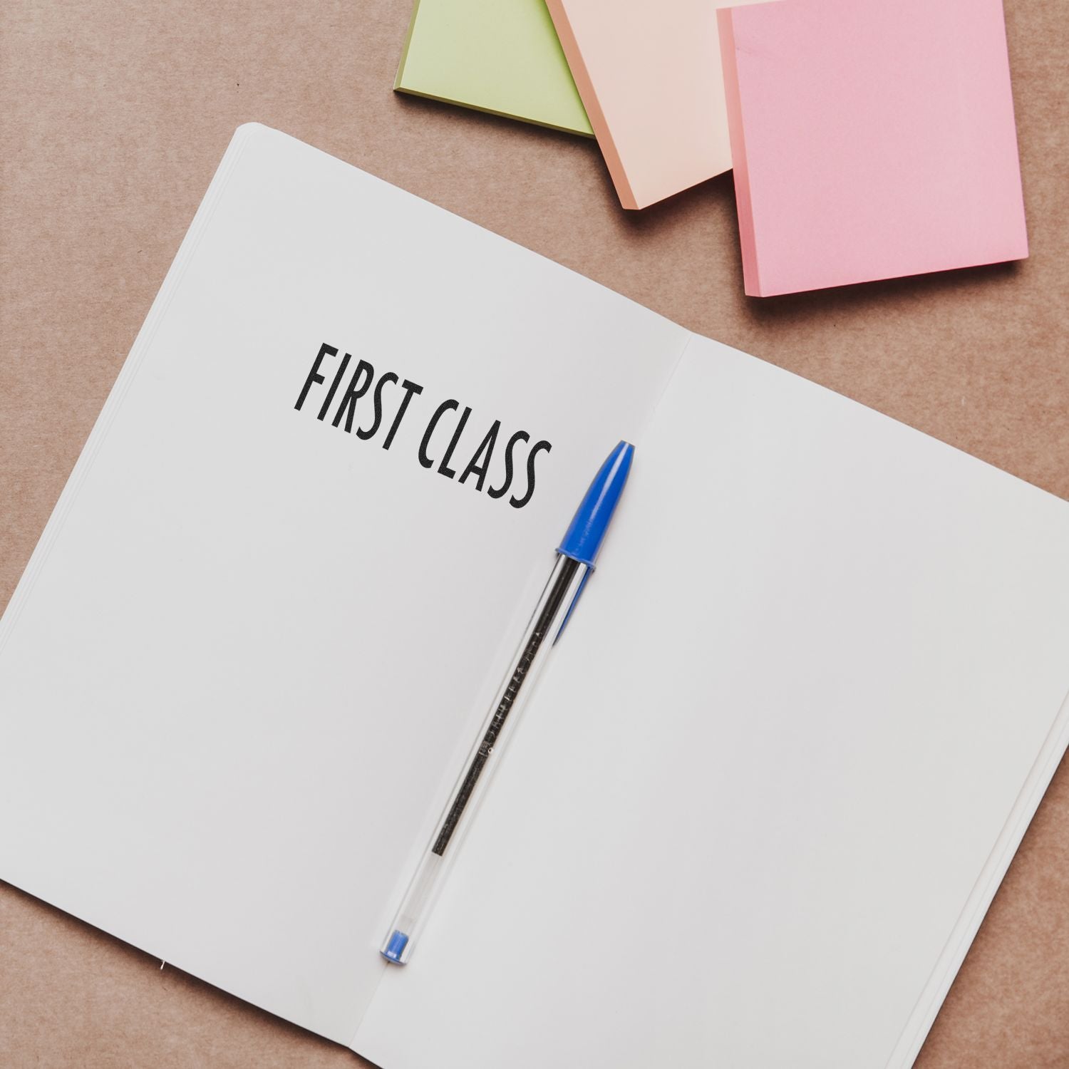 Large Self Inking First Class Stamp used on an open notebook with a blue pen and colorful sticky notes in the background.