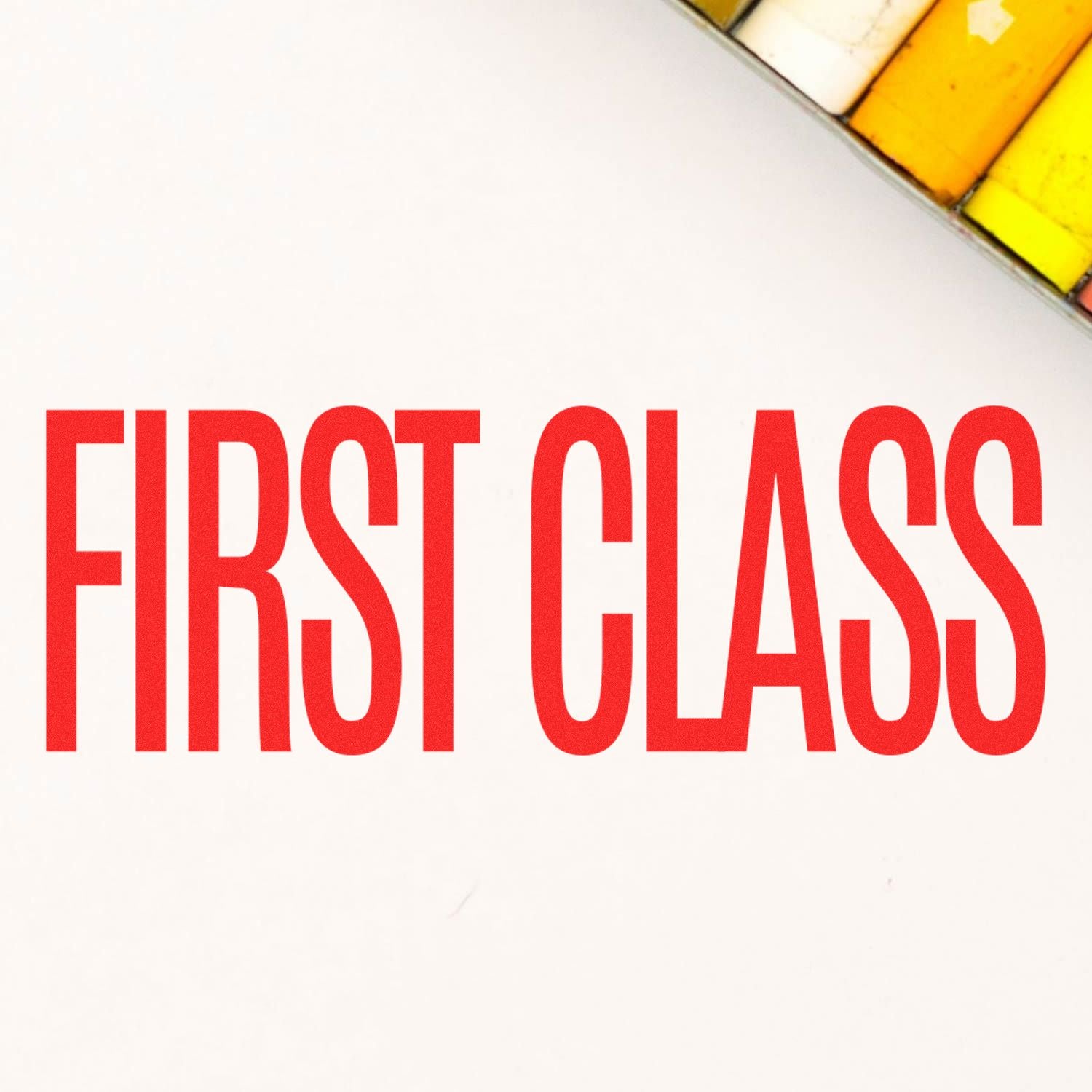 Large First Class Rubber Stamp imprint in bold red letters on white paper, with a glimpse of a yellow and white object in the corner.