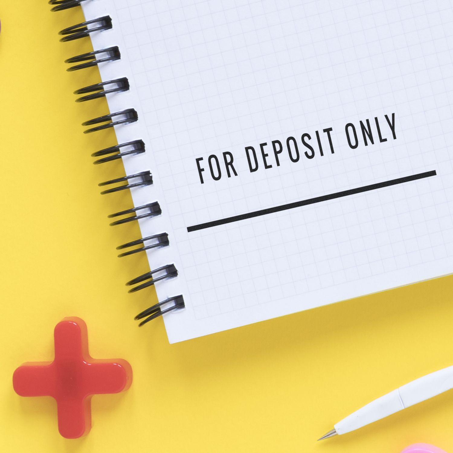 Large Self Inking For Deposit Only with Line Stamp used on a spiral notebook, placed on a yellow surface with a pen and red cross nearby.